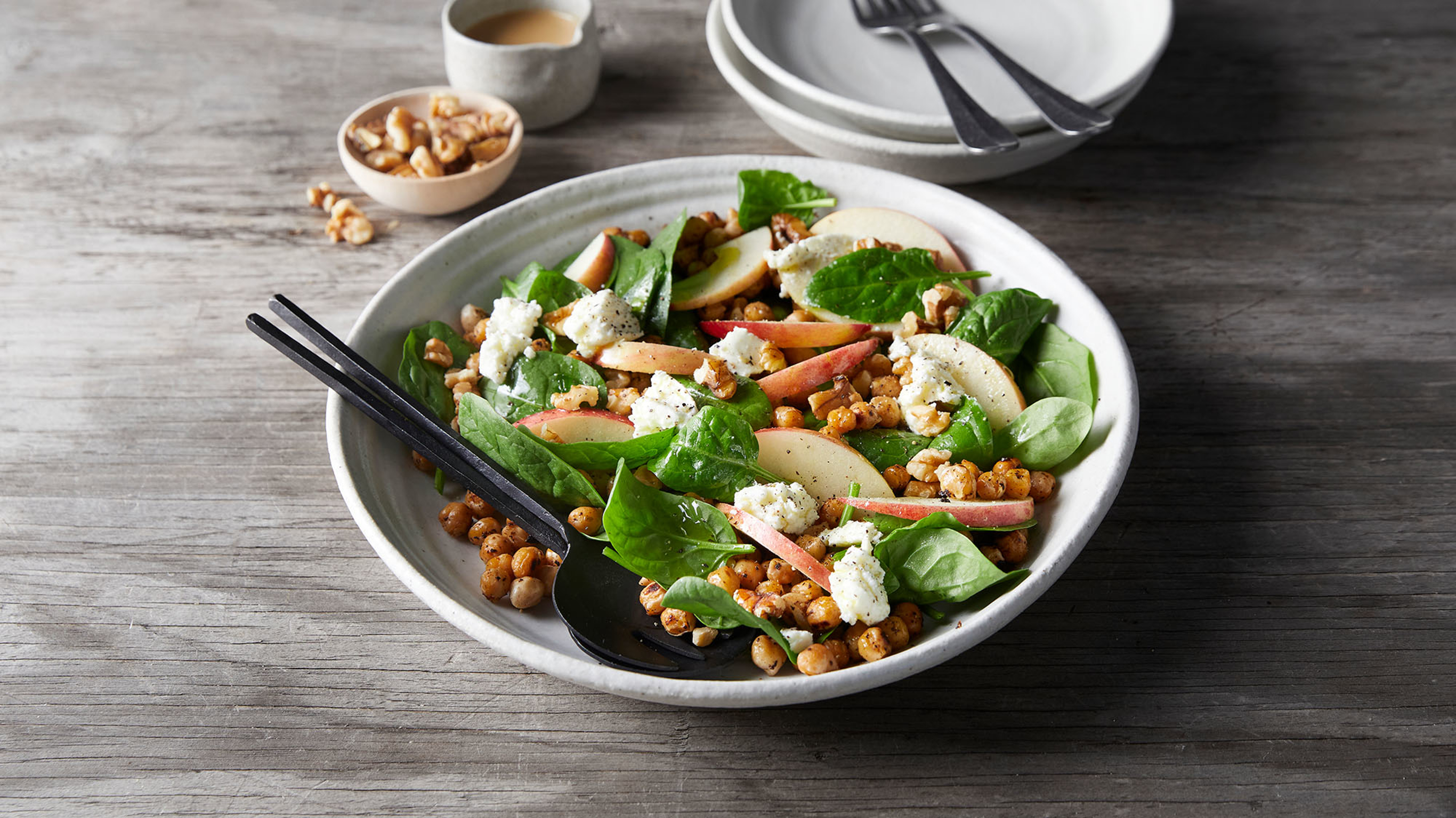 A bowl of Centr's Chickpea, Apple & Walnut Salad with Goat’s Cheese sits on a grey wooden table, ready for eating.