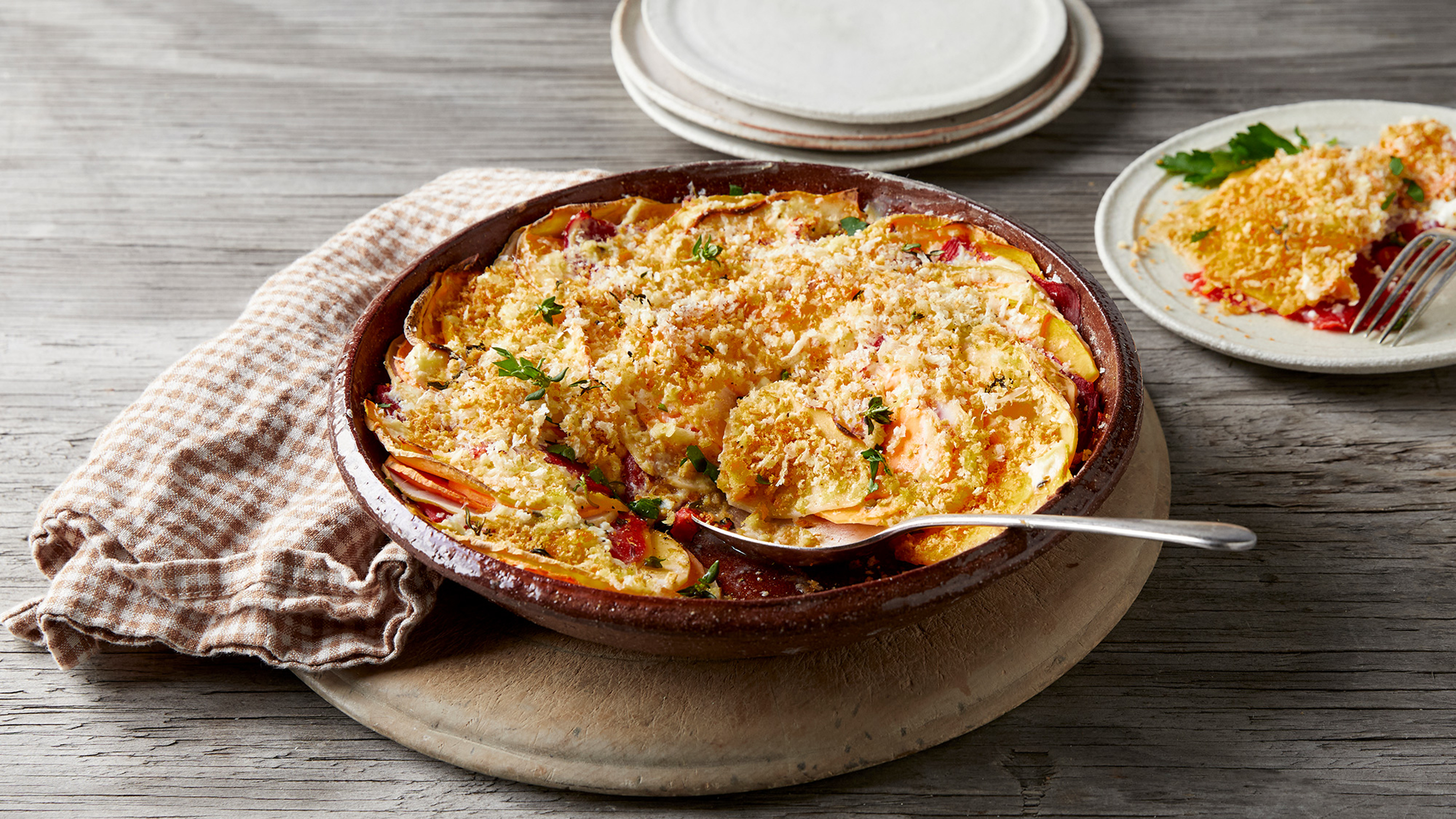 A dish of Colourful Vegetable Gratin rests on a wooden board, ready for serving.