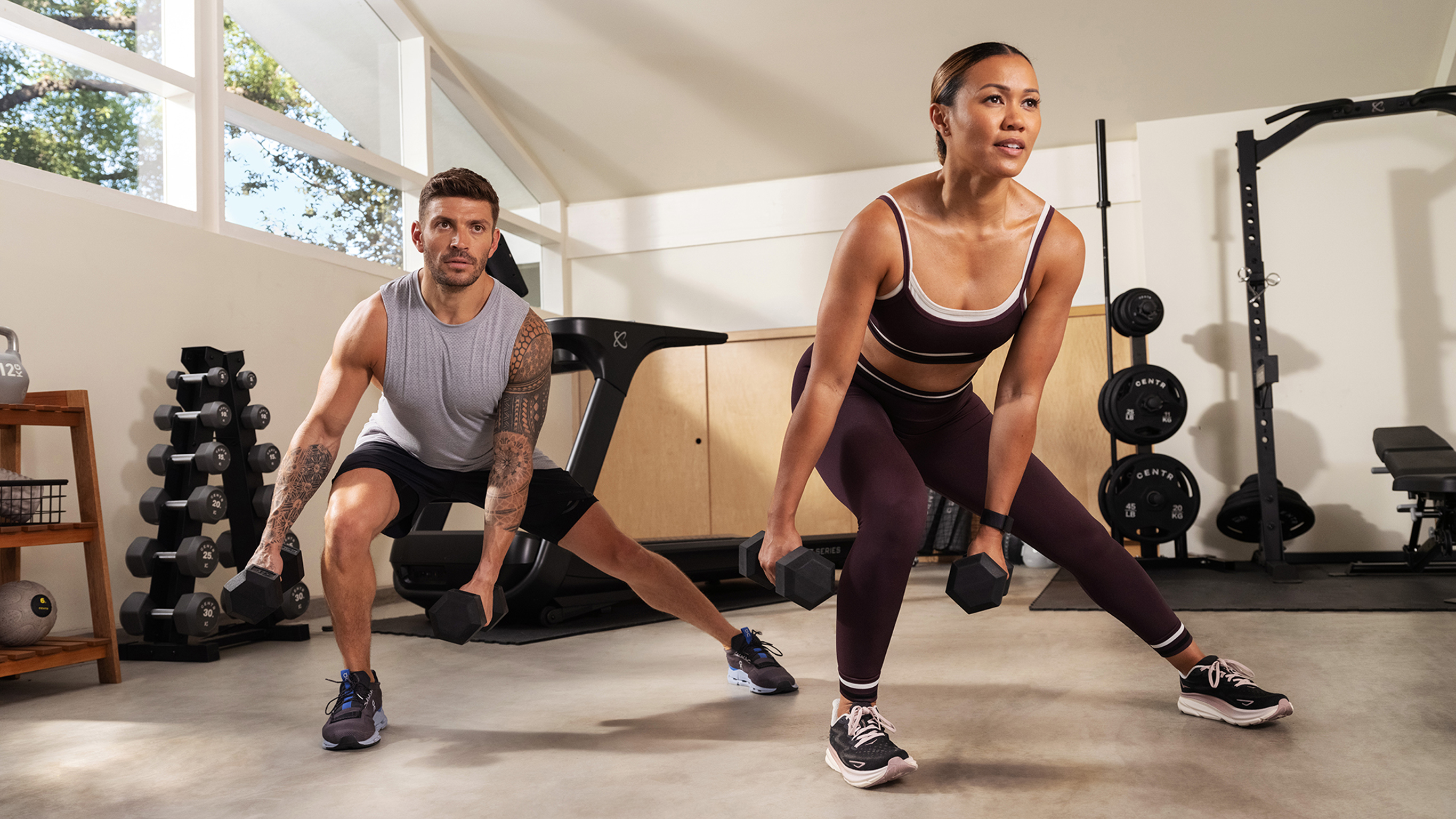 Centr trainers Luke Zocchi and Maricris Lapaix perform a dumbbell lateral lunge exercise.