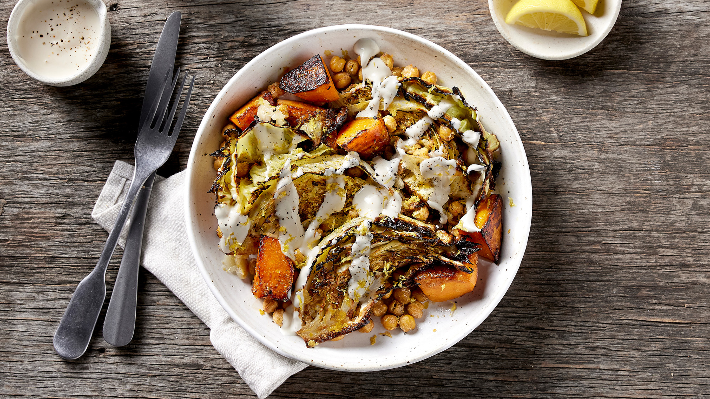 An overhead photo of a plate of Charred Cabbage & Pumpkin Salad with Tahini Dressing sitting on a wooden table, with knife and fork on the side.