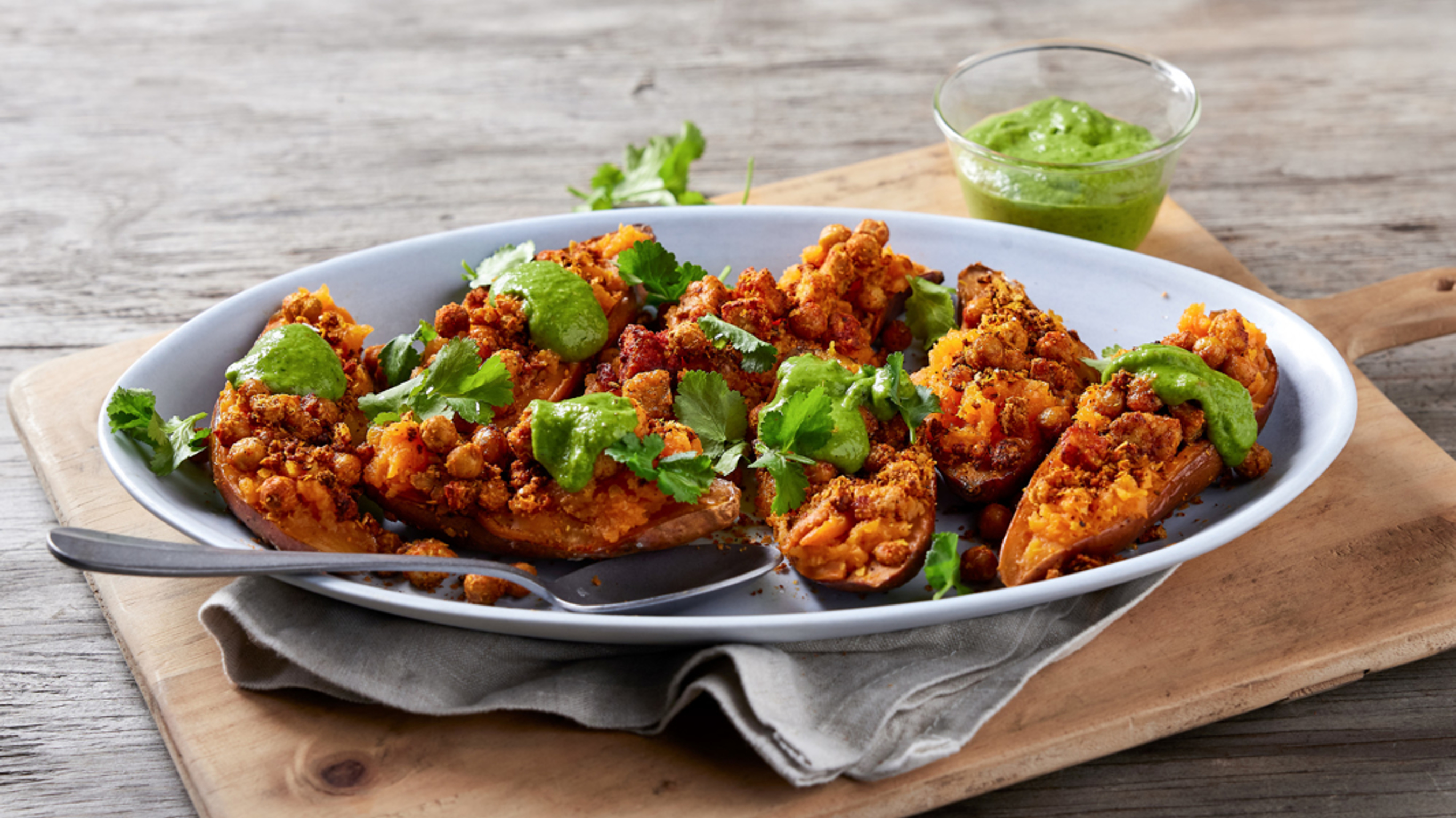 A platter of Masala Chickpea Stuffed Sweet Potato sits on a wooden table, ready for serving.