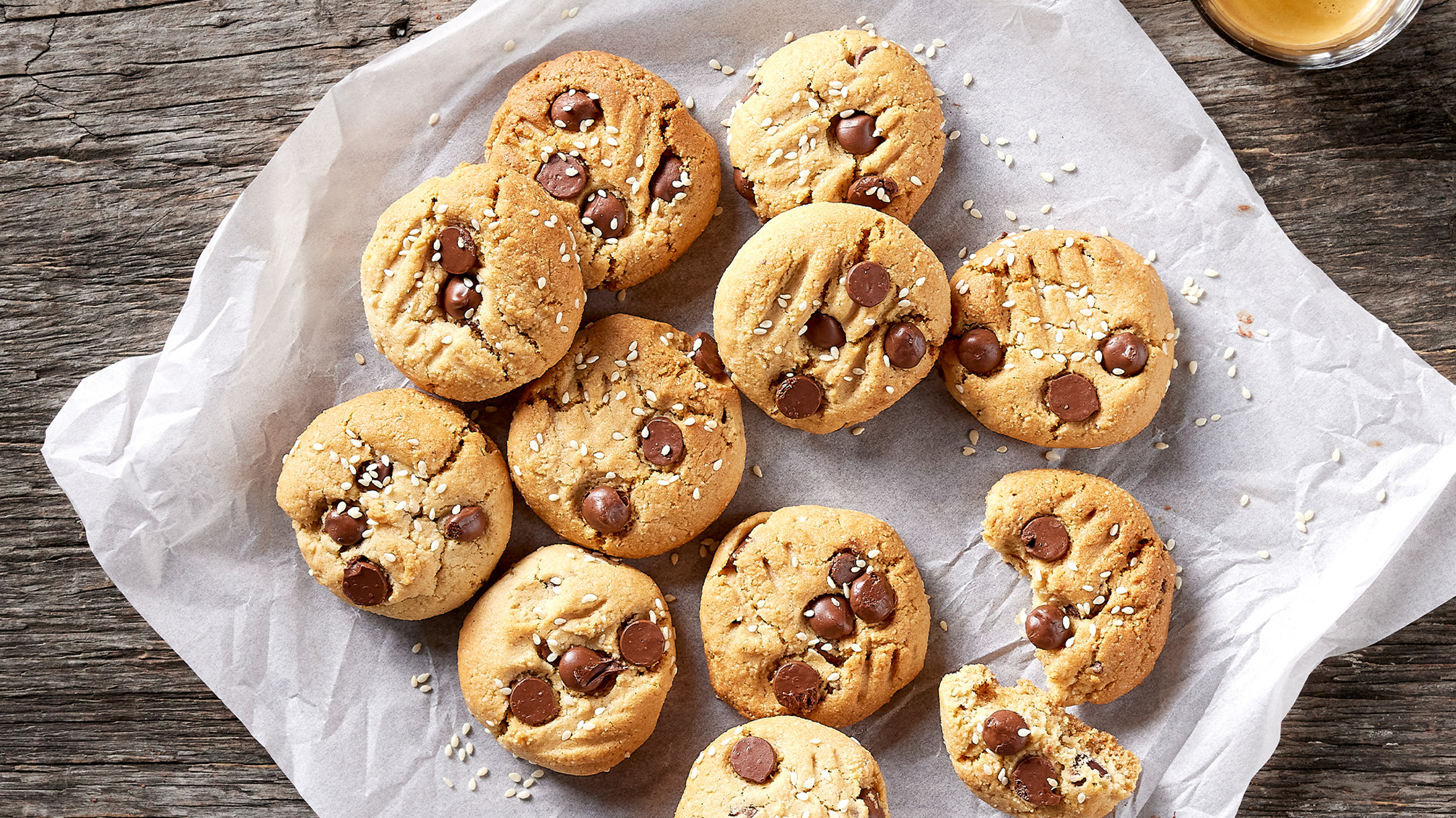 Freshly baked Tahini & Choc Chip Cookies sit on baking paper on a plate, ready to eat.