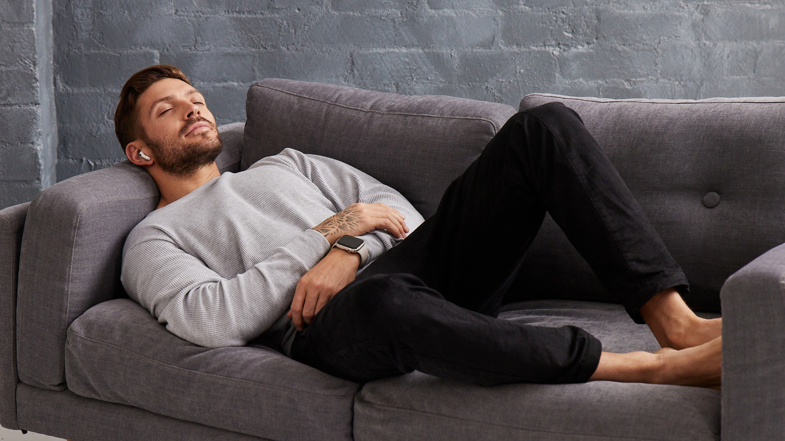 Luke Zocchi sleeps on a couch listening to a meditation on Centr through wireless headphones.