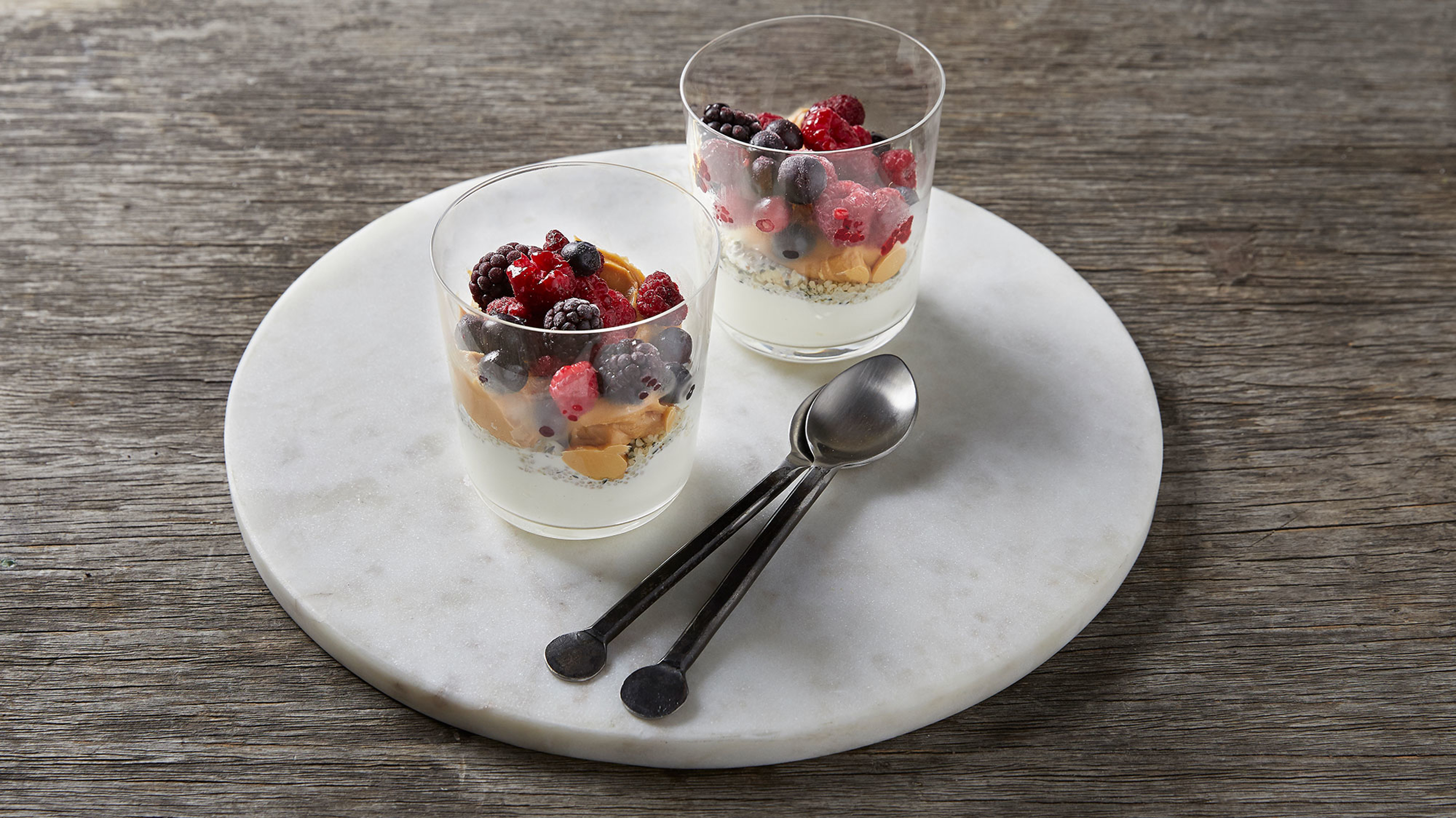 Two serves of Power Protein Yogurt with Peanut Butter sit on a round marble serving board, ready for eating.