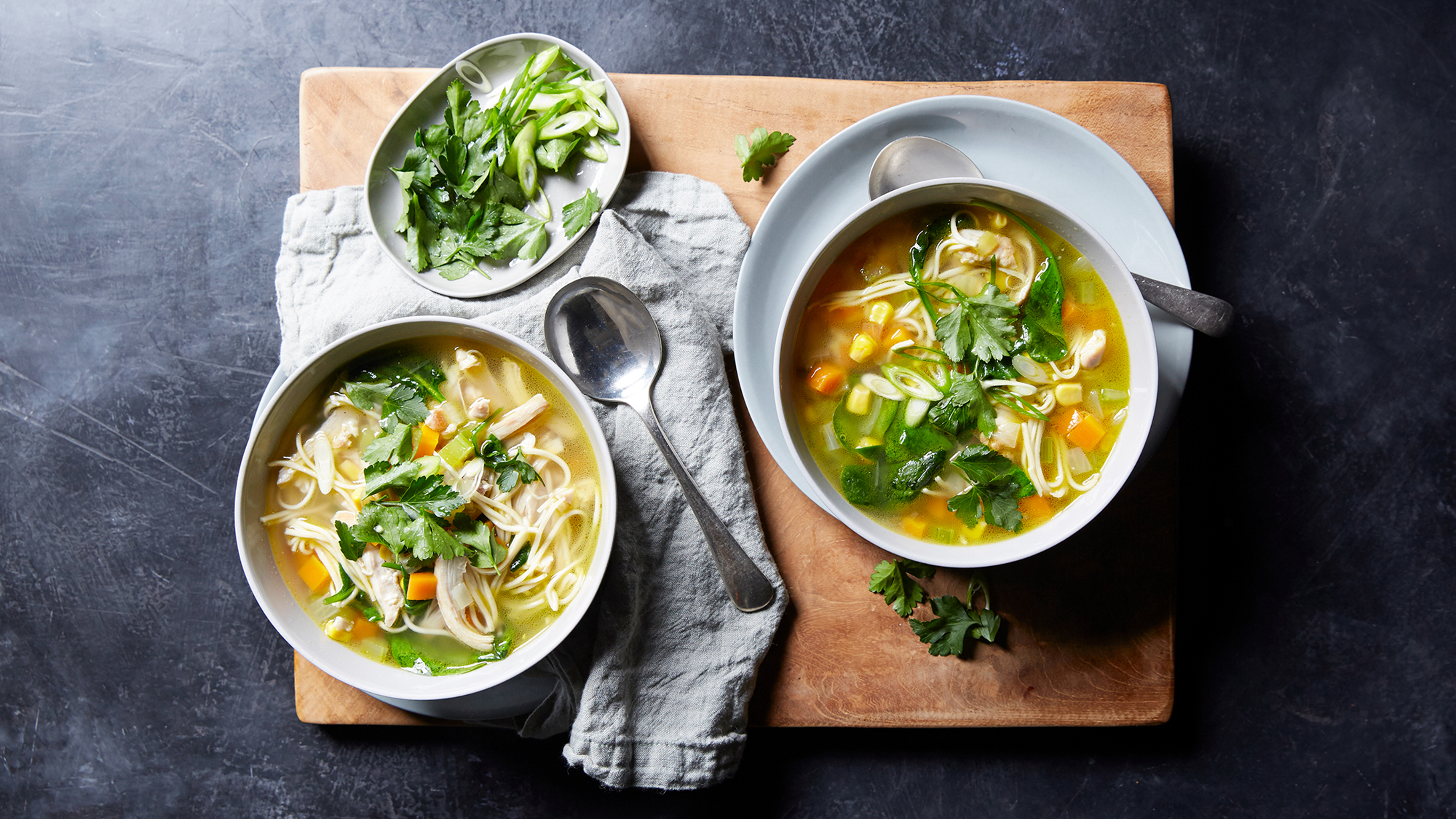 Two bowls of Centr's Wholesome Chicken Soup sit on a wooden serve board, ready for eating.