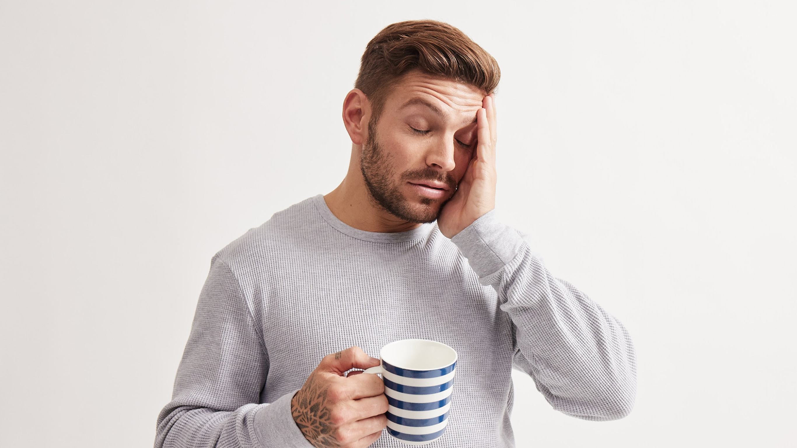 Luke Zocchi rubs the side of his head while sleepily holding a cup of hot drink.