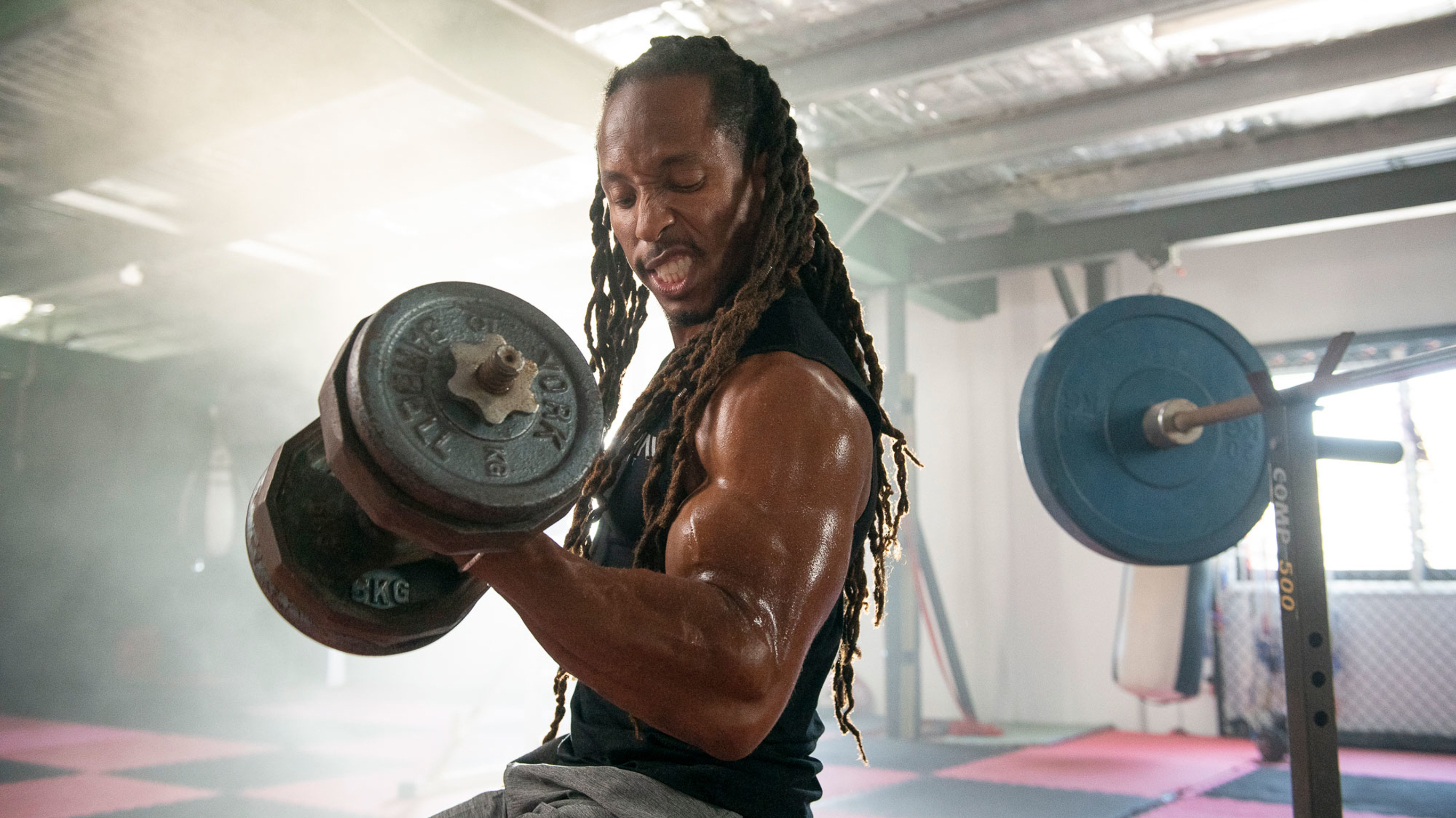 A bodybuilder doing a dumbbell curl and snarling.