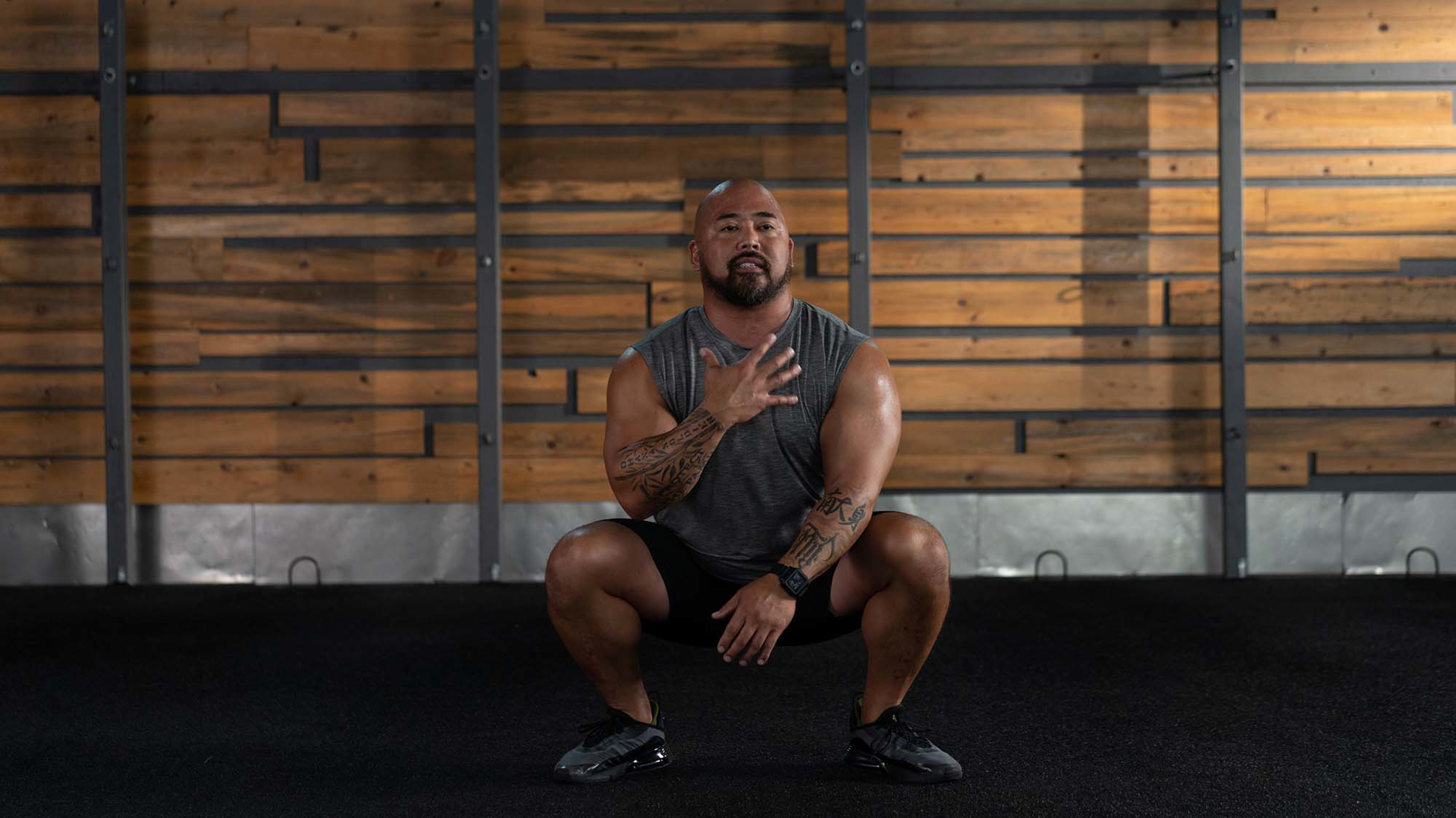 A man sits in a deep squat with one hand over his chest.