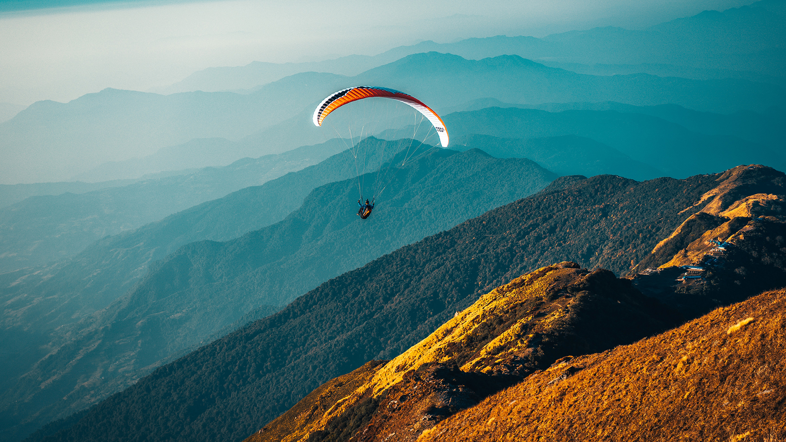A person paraglides over a mountain range.