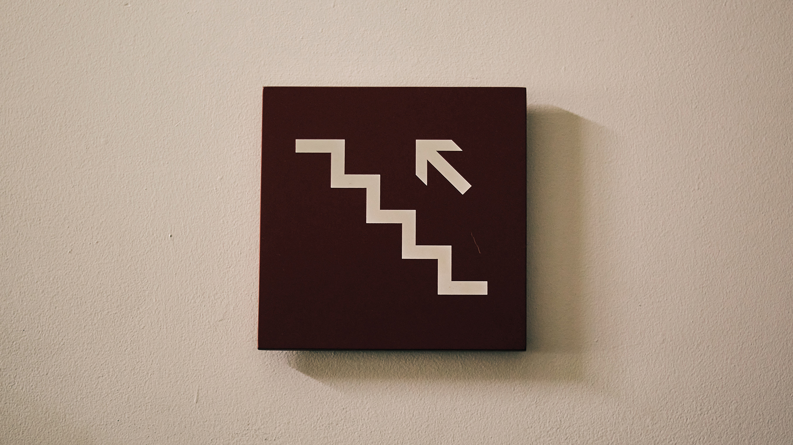 A brown sign with an arrow pointing up a staircase.
