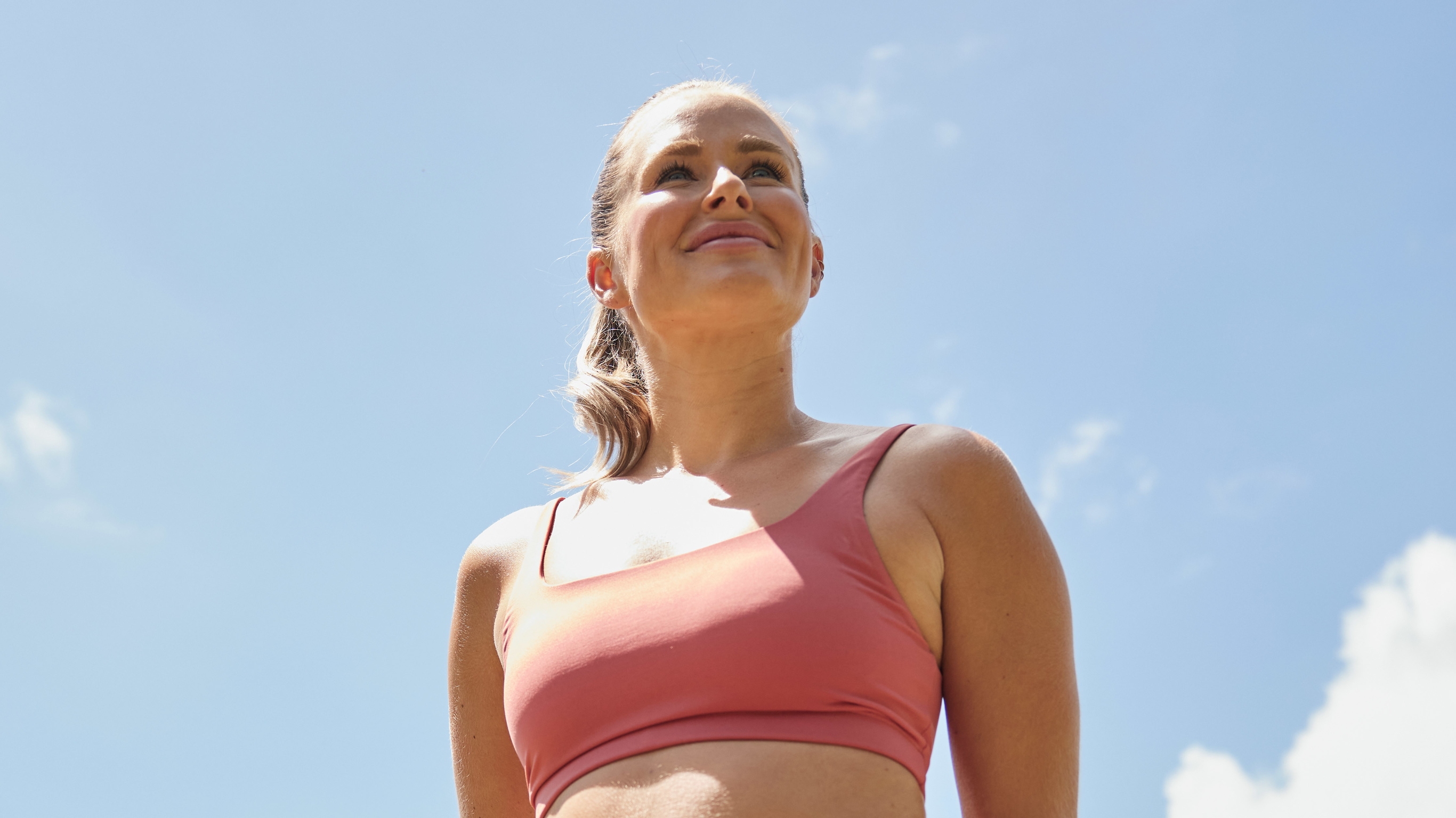 Alexz Parvi, smiling and wearing pink activewear, with a blue sky behind her