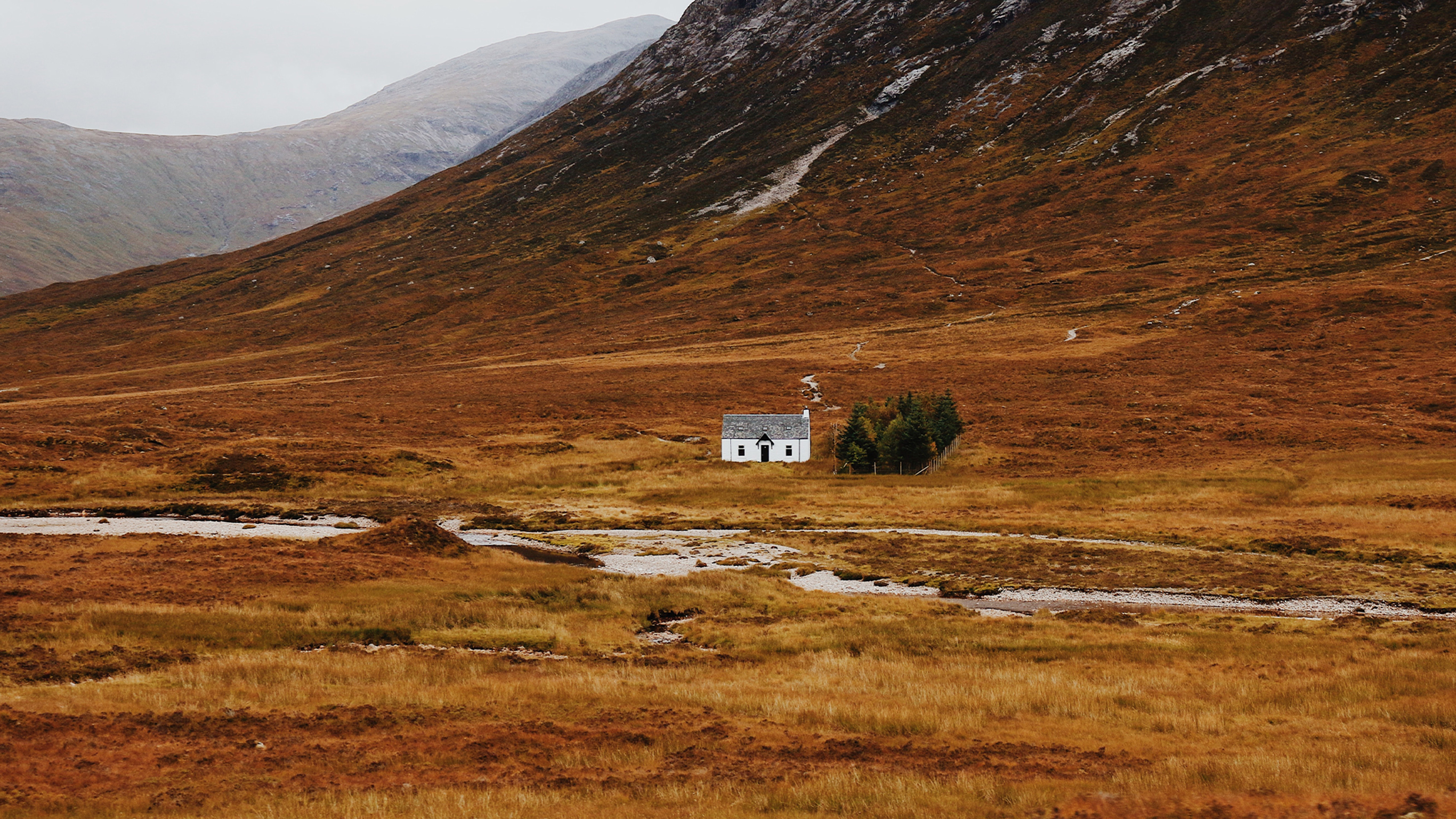 A small, isolated white and grey cottage at the foot of a mountain.