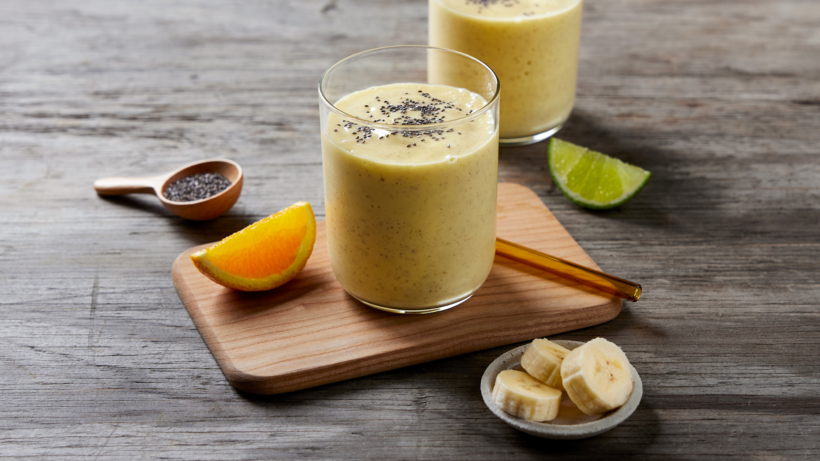 An aerial view of two glasses of golden Pineapple, Coconut and Turmeric Smoothie sit on a wooden table with pineapple slices and a spoonful of turmeric on the side.