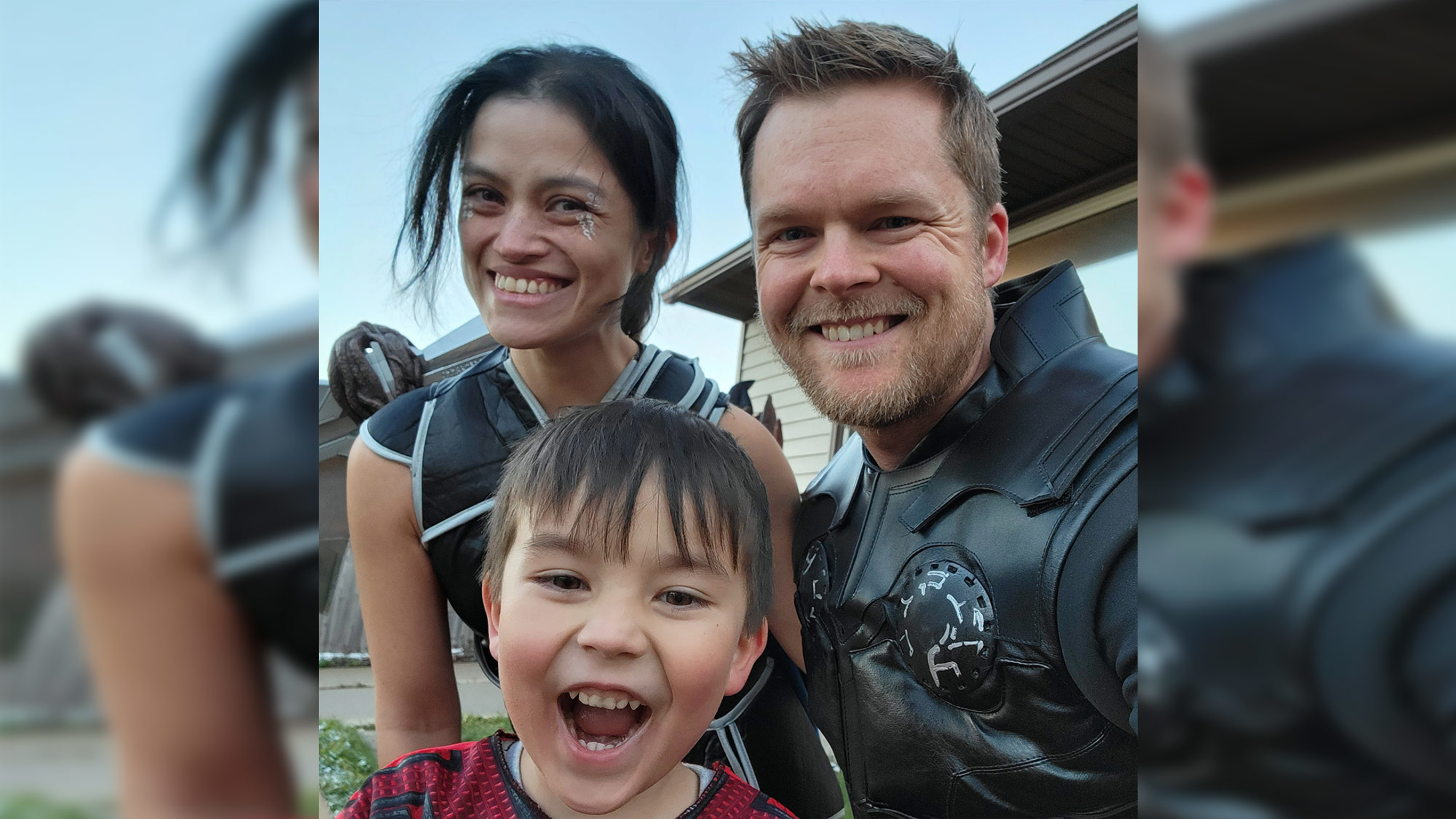 A photo of Mark Haverland with his wife and young son. All three are smiling and wearing superhero costumes.