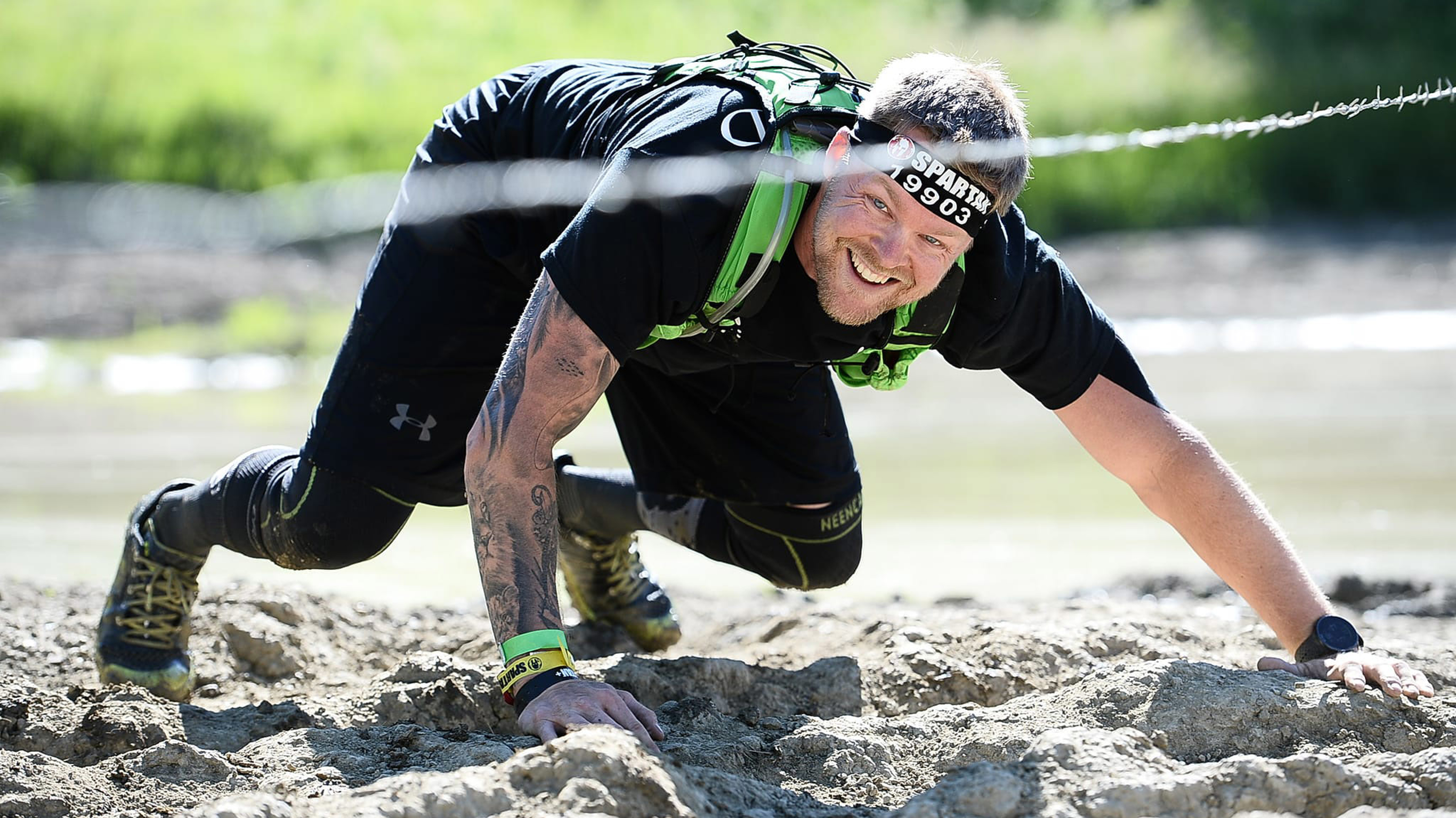 Centr member Mark Haverland, smiling and wearing black workout clothes, does a bear crawl through mud during an endurance event.
