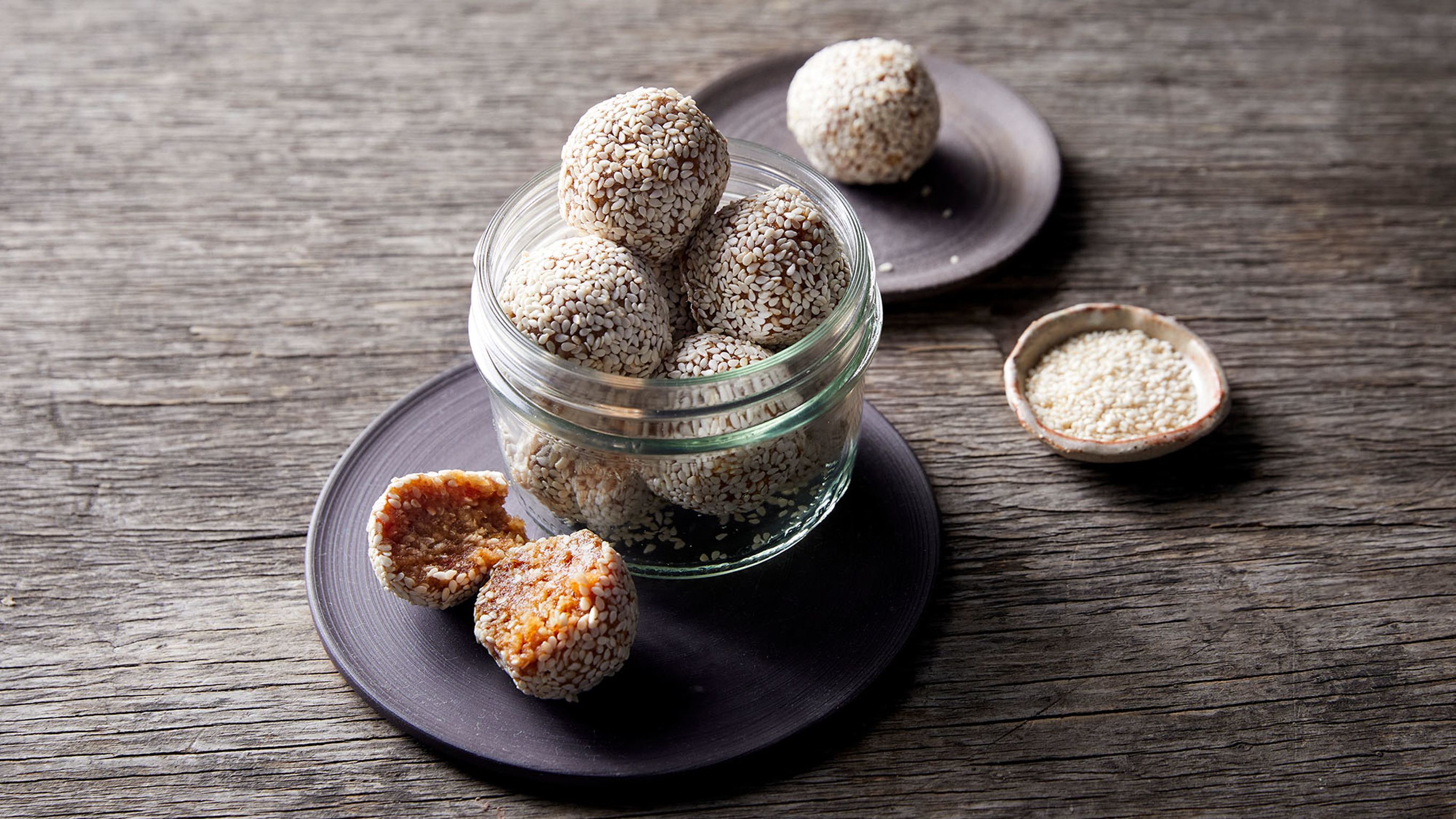 A glass jar full of Date, Cashew & Sesame Bliss Balls from the Centr recipe library sits on a table.