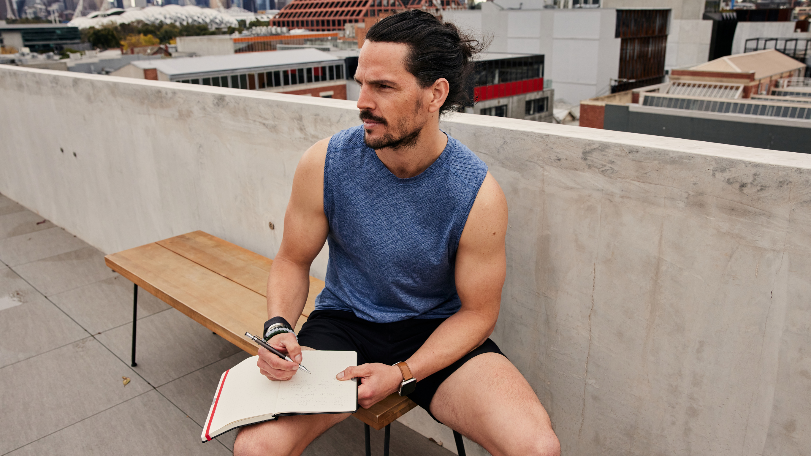 Centr chef and beginner fitness trainer Dan Churchill sits on a rooftop bench and writes in his journal, in order to relieve stress and cut down on his screen time.