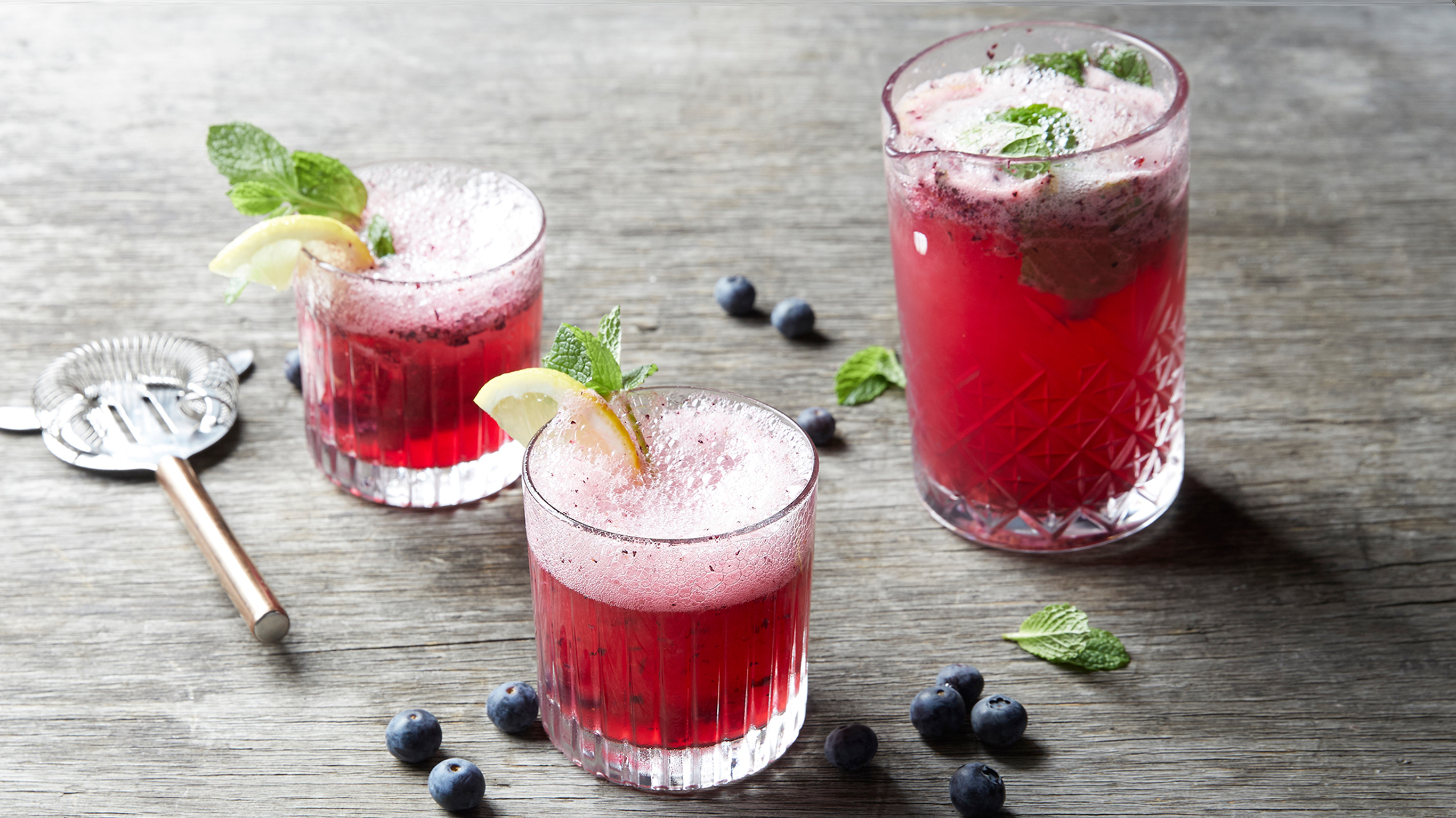 Three glasses of the non-alcoholic Blueberry Lemon Spritzer from the Centr recipe library sit on a table.
