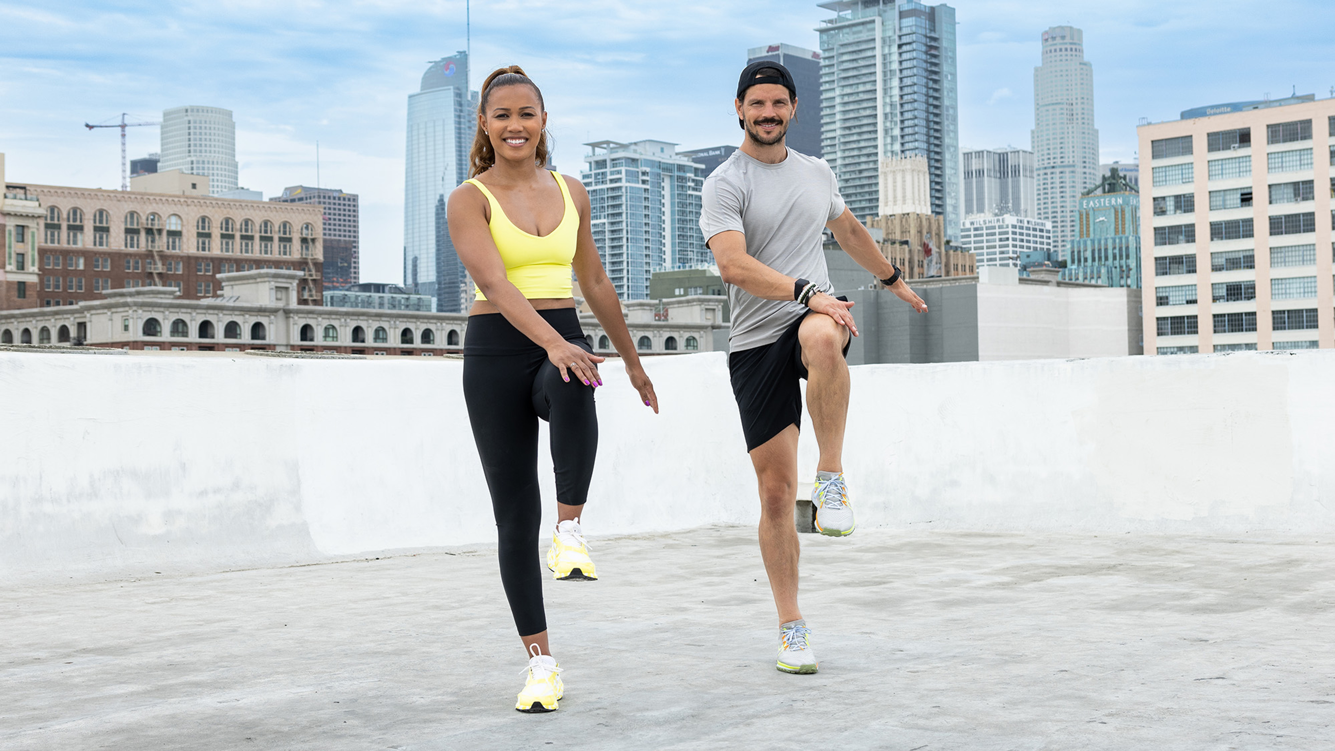 Maricris Lapaix and Dan Churchill perform the easy, beginner-friendly high knee exercise on a rooftop.