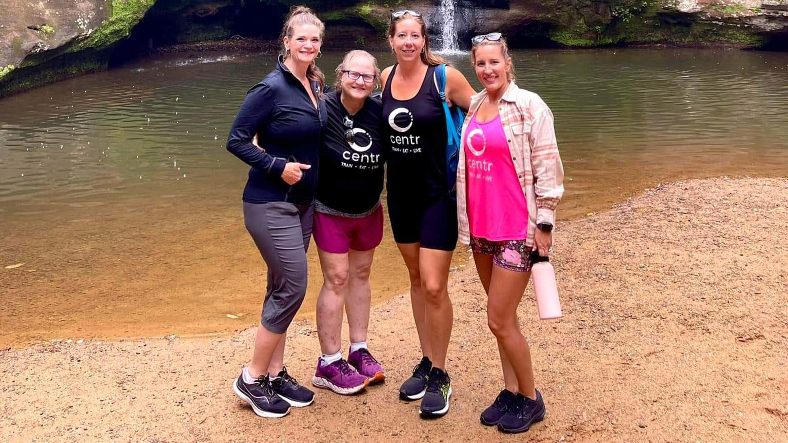 Christine and some friends from the Centr community stand in front of a small lake, looking fit and happy.