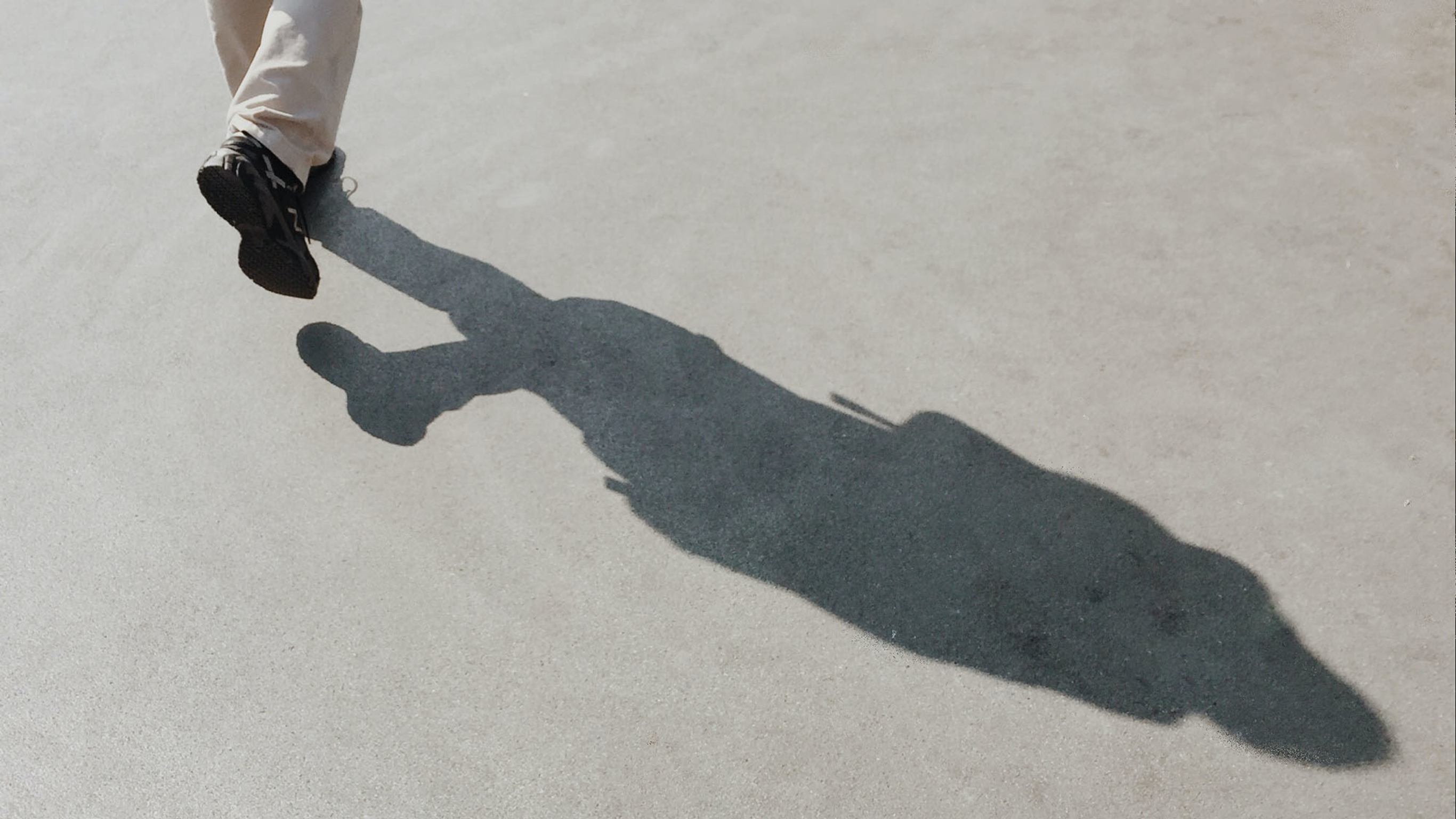 A man’s shadow seen on the ground as he is walking and listening to a guided meditation walk from Centr.