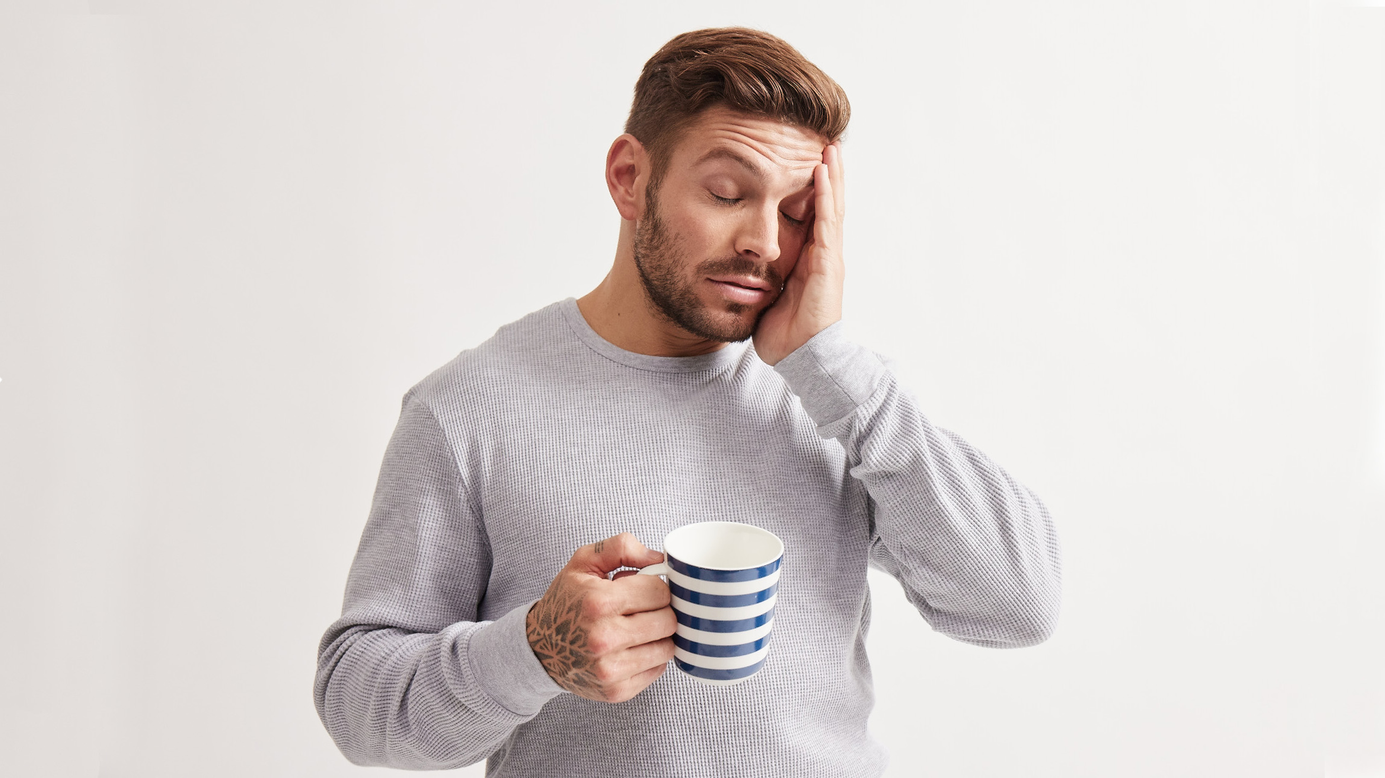 A tired Luke Zocchi rubs his face while holding a coffee mug.