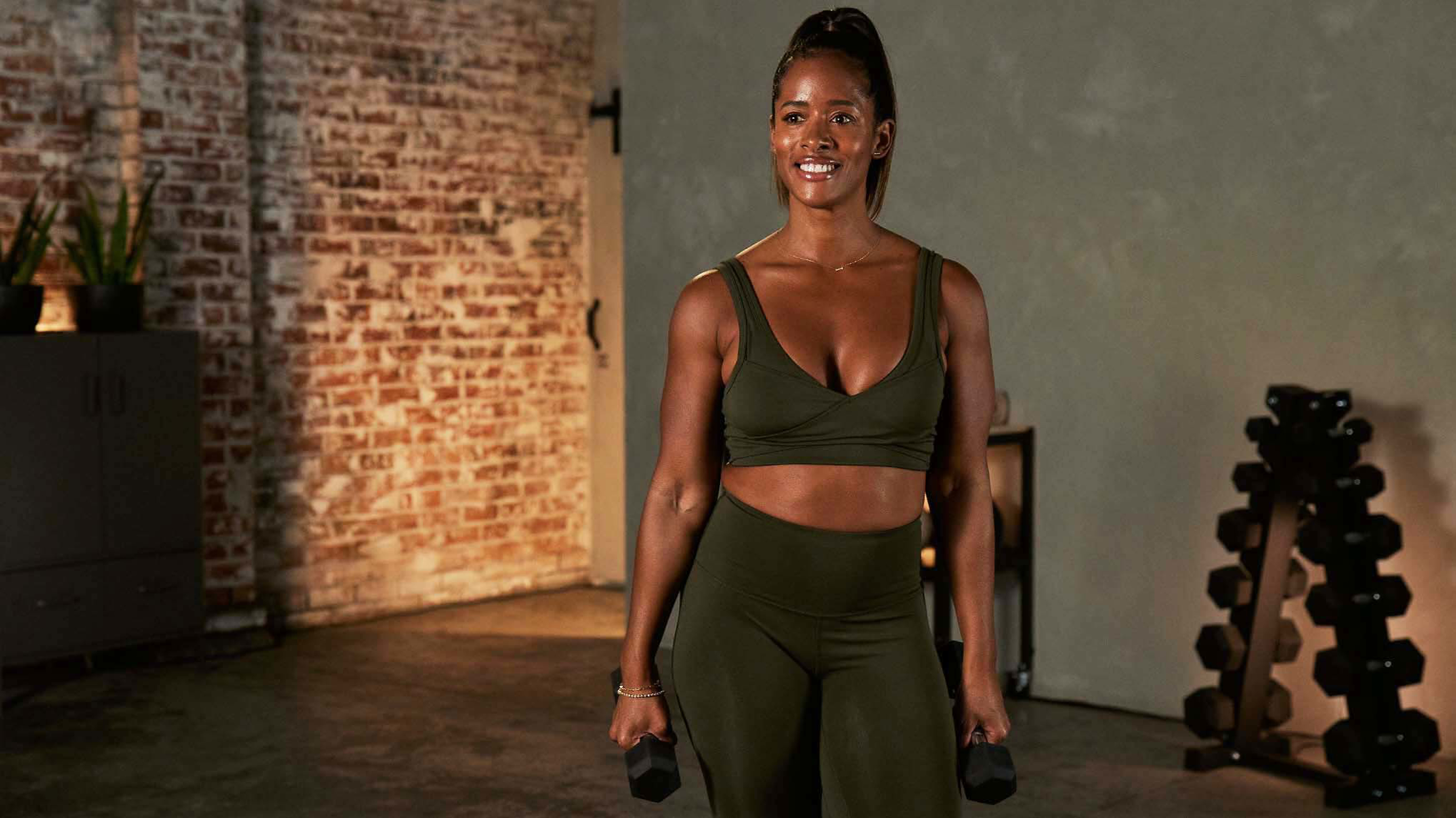 Ingrid Clay smiles while holding a dumbbell in each hand.