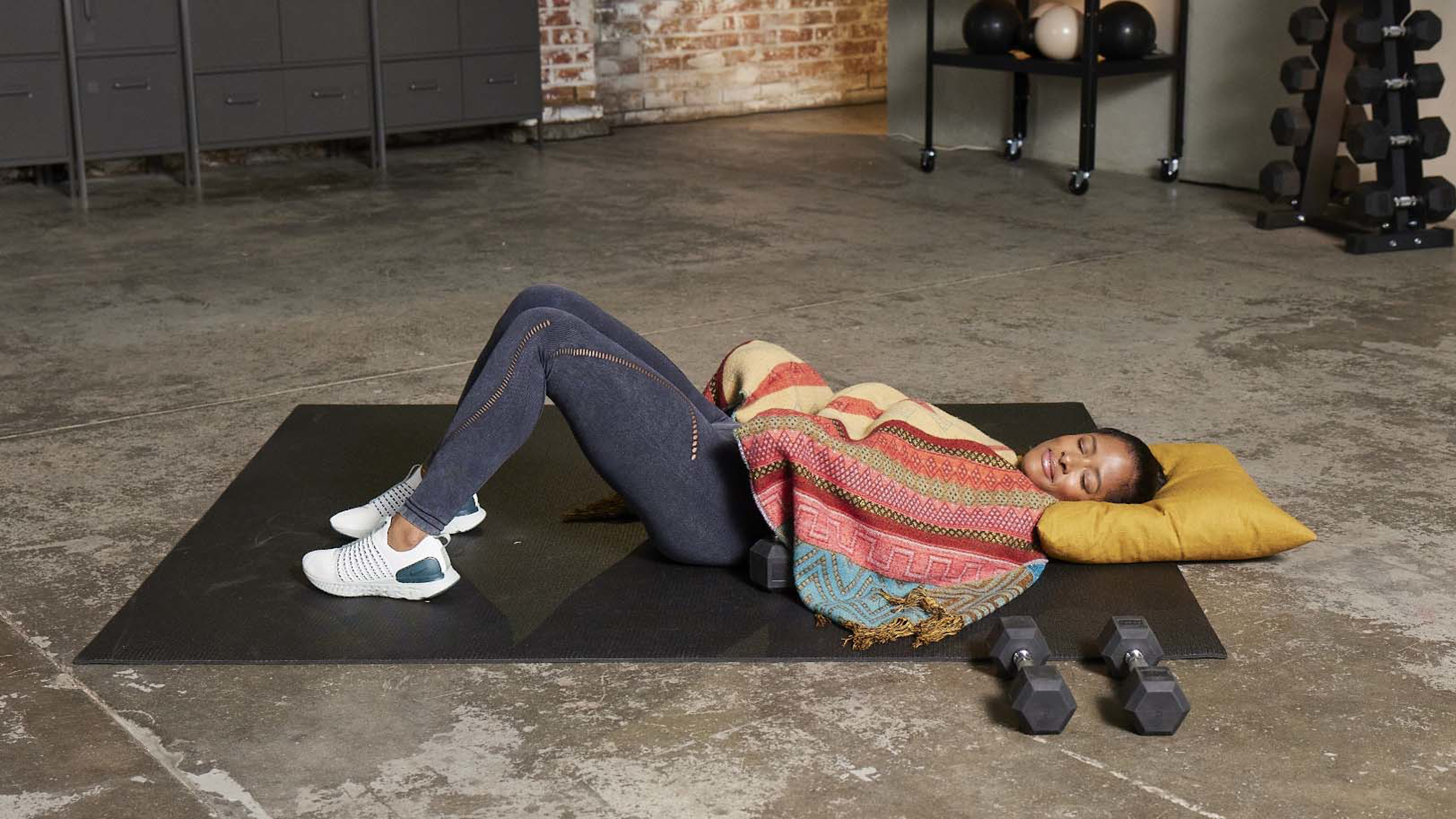 Ingrid Clay lies down on a workout mat with a blanket, ready to take a nap in between filming workouts for Centr.