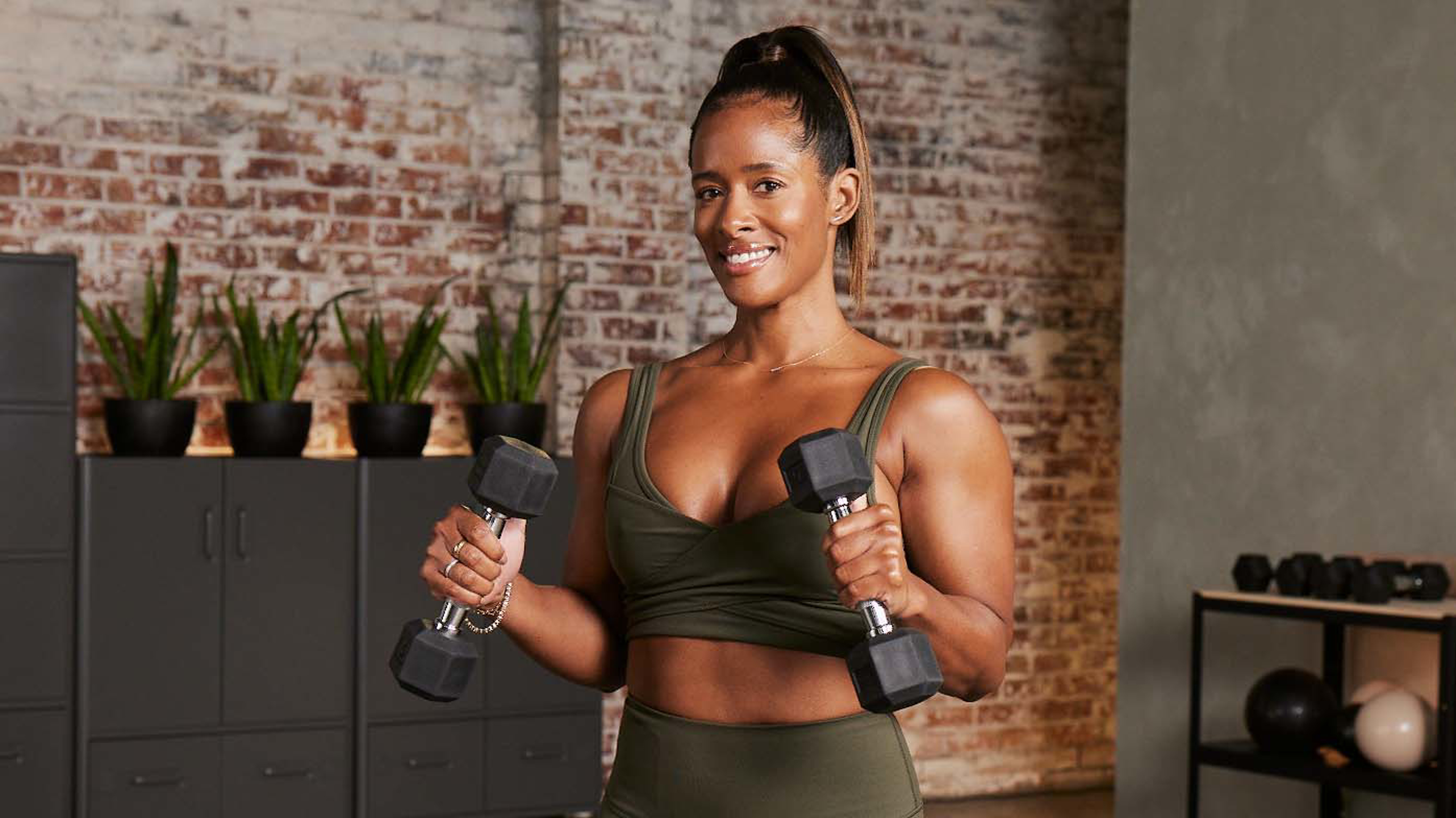 Centr trainer and strength expert Ingrid Clay smiles while holding a dumbbell in each hand.