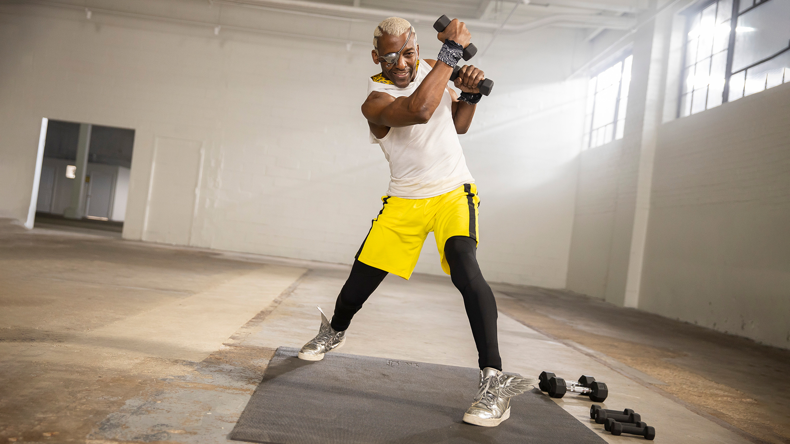 Centr boxing trainer Michael Olajide Jr., wearing yellow shorts and a white singlet top, shadow boxes with a dumbbell in each hand.