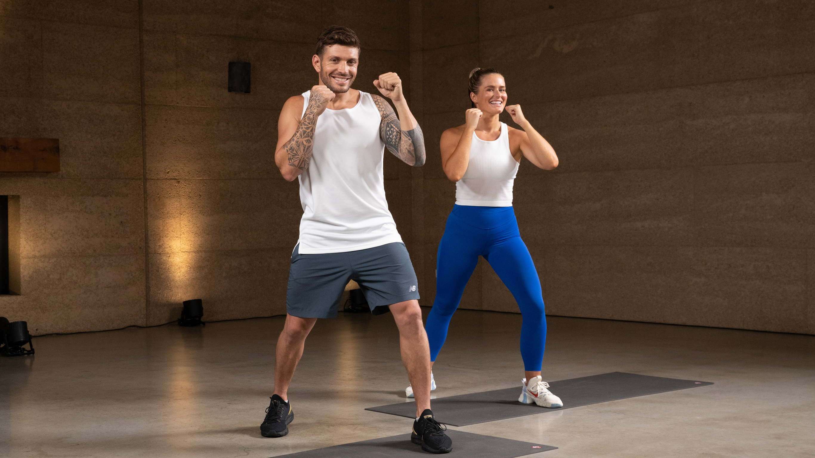 Luke Zocchi and Alexz Parvi stand side-by-side and strike a fists-up boxing style, in the workout studio.