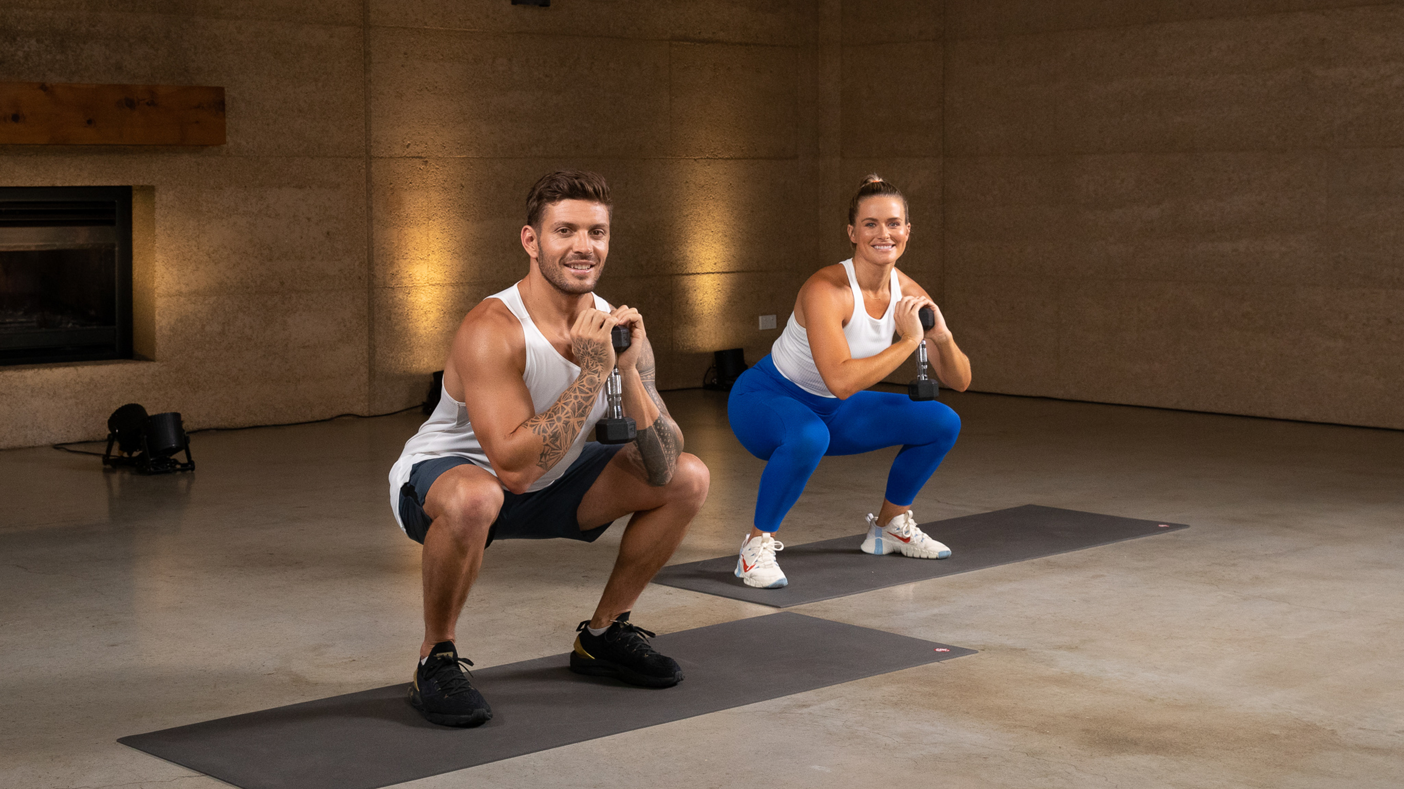 Luke Zocchi and  Alexz Parvi perform a dumbbell goblet squat side by side in the gym studio.