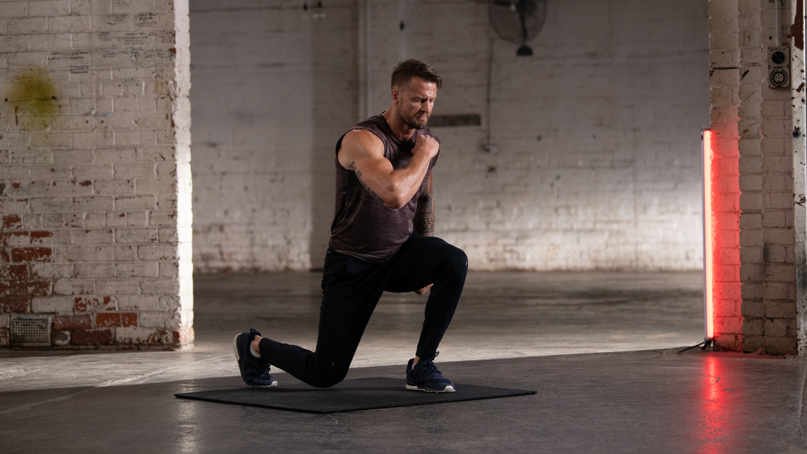 Centr trainer Bobby Holland Hanton  performs a forward lunge, inside an old warehouse space, as part of a plyometric workout.