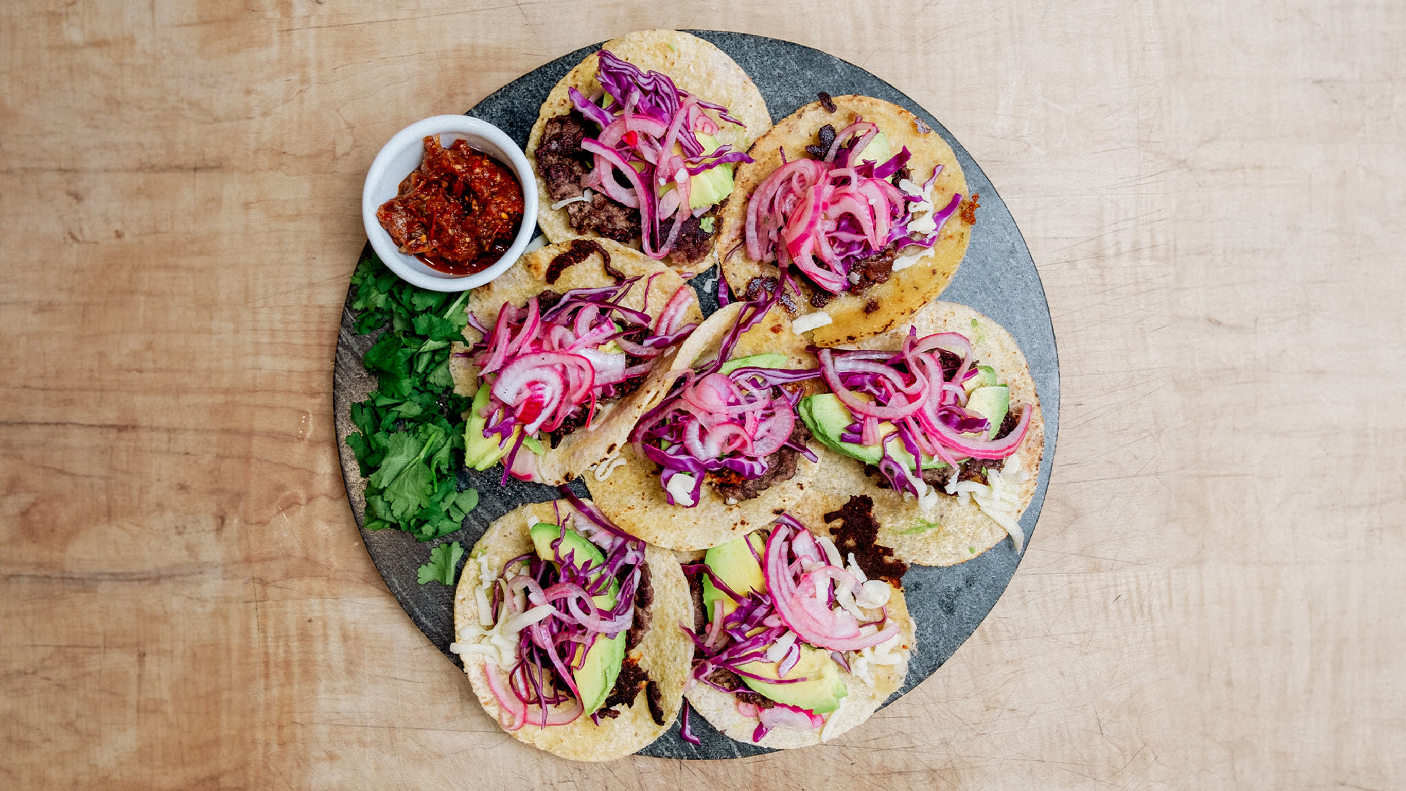 A round platter of smashed beef tacos piled up, and a small side bowl of chilli dip.
