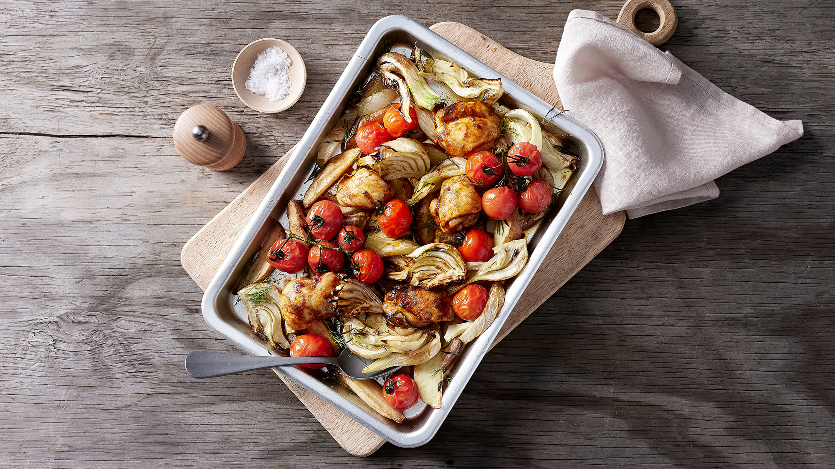A tray of Chicken, potato and fennel bake in a metal cooking pan sits on a table.