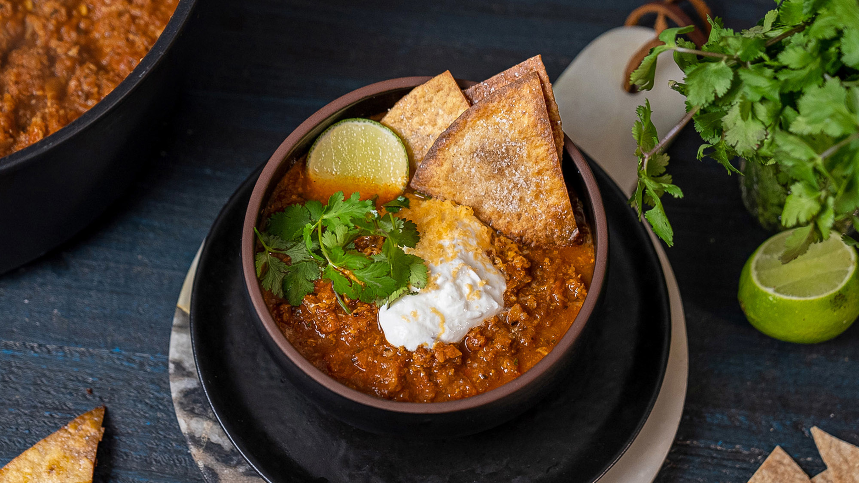 A bowl of turkey chilli and tortillas sits on a table.