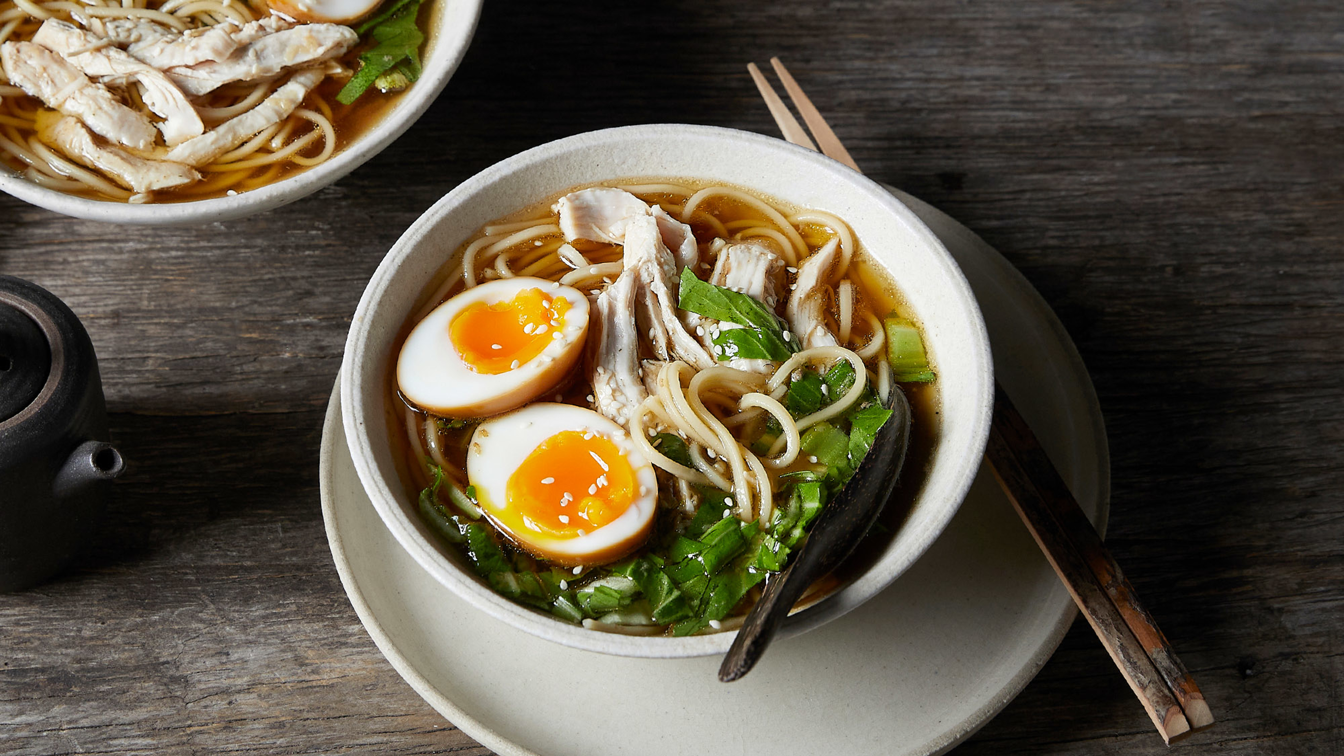A bowl of Simple Chicken Ramen in a bowl on plate, sits on a table.