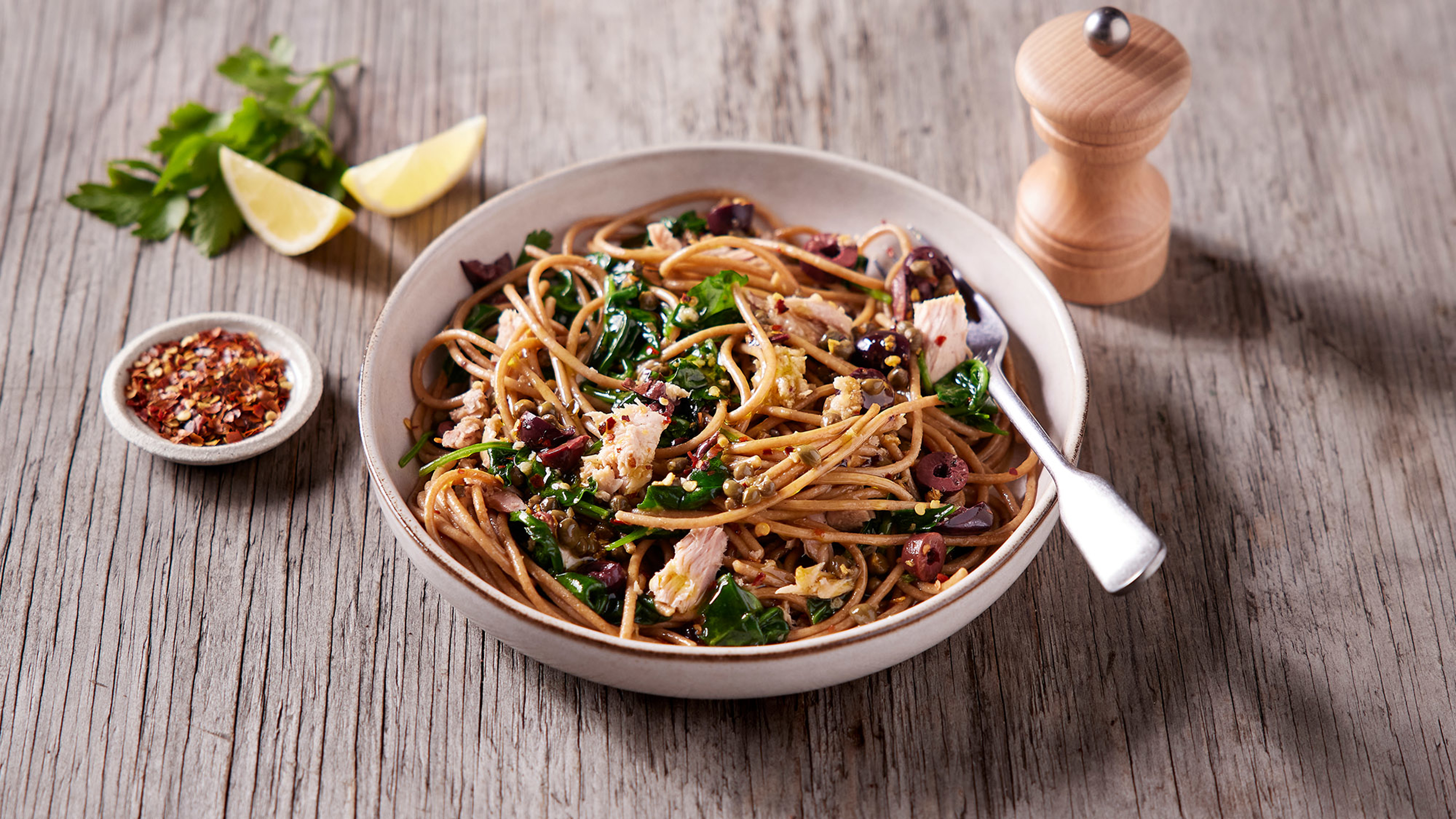 A bowl ot Tuna Puttanesca Pasta, in a white pasta bowl, sits on a table.