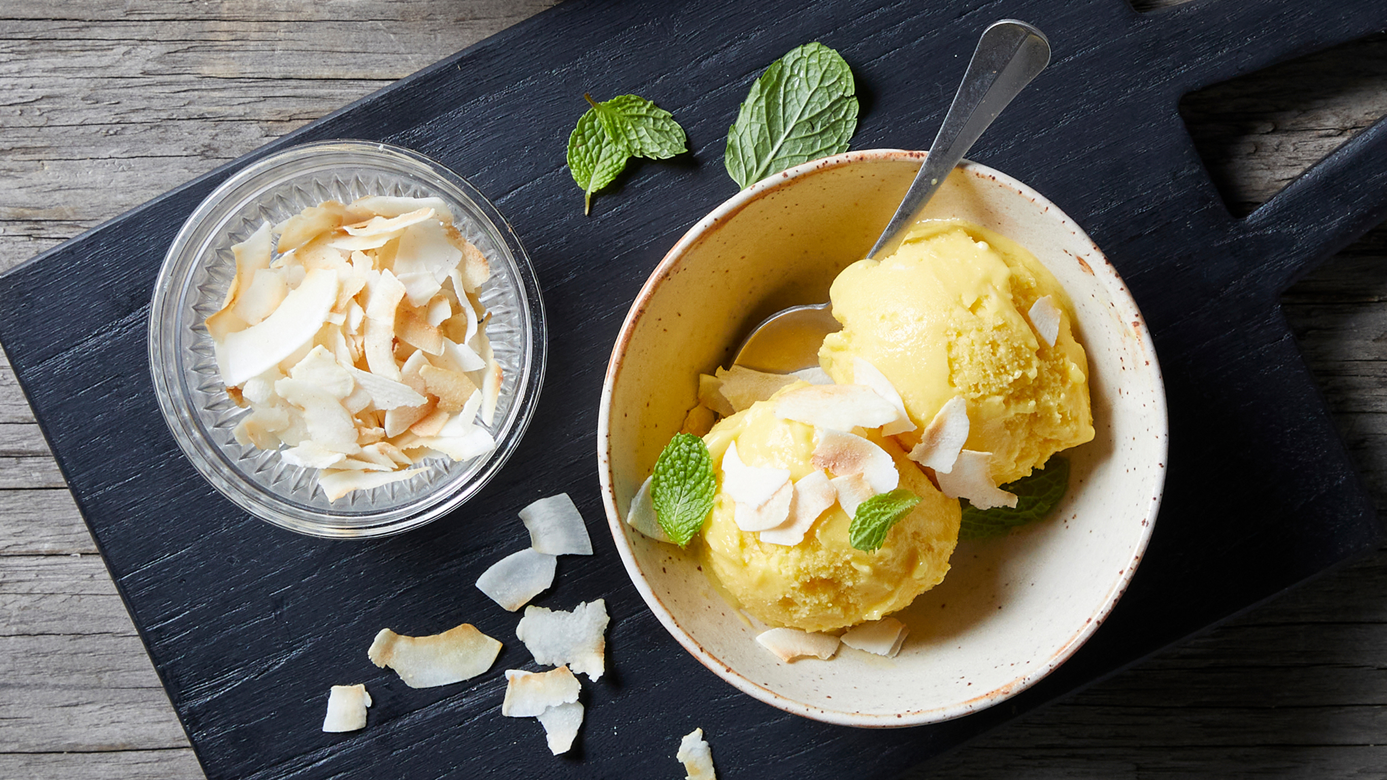 A bowl of 2-ingredient Mango Sorbet, from the Centr meal plan, sits on a table alongside some condiments.
