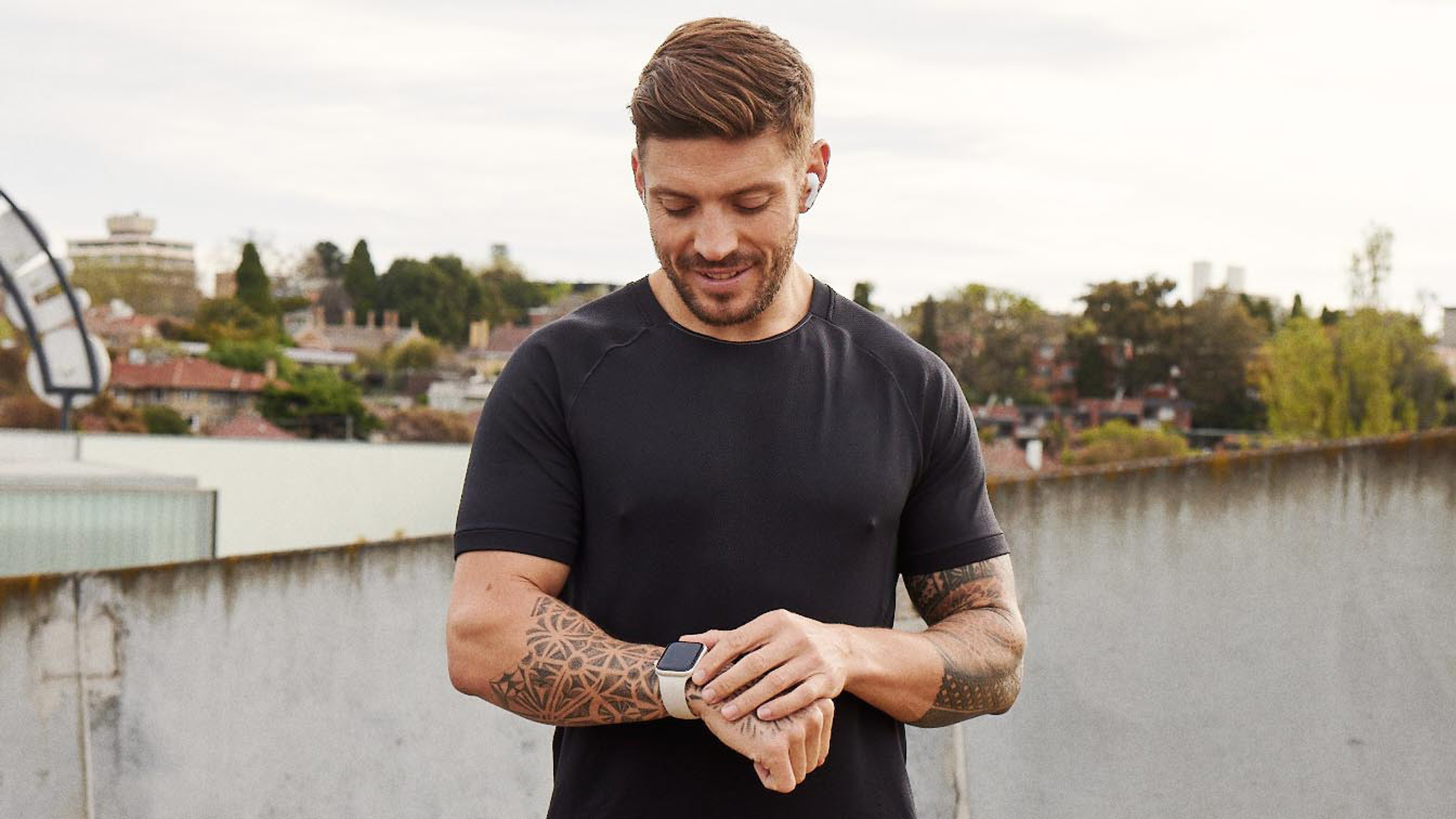 Centr trainer Luke Zocchi looks down at his fitness watch, while standing outside in an urban setting.