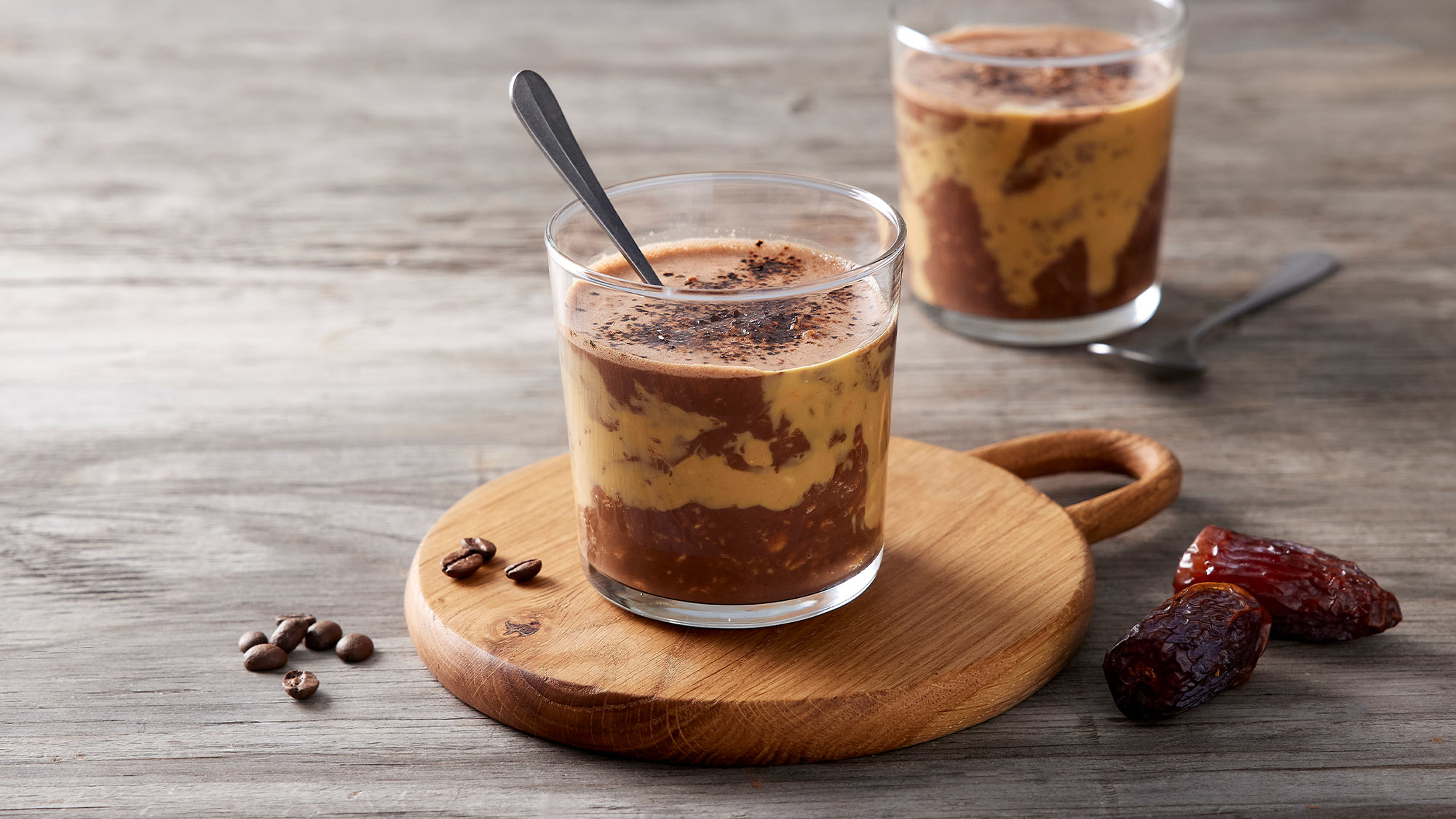 A glass of mocha overnight oats sits on a wooden board.