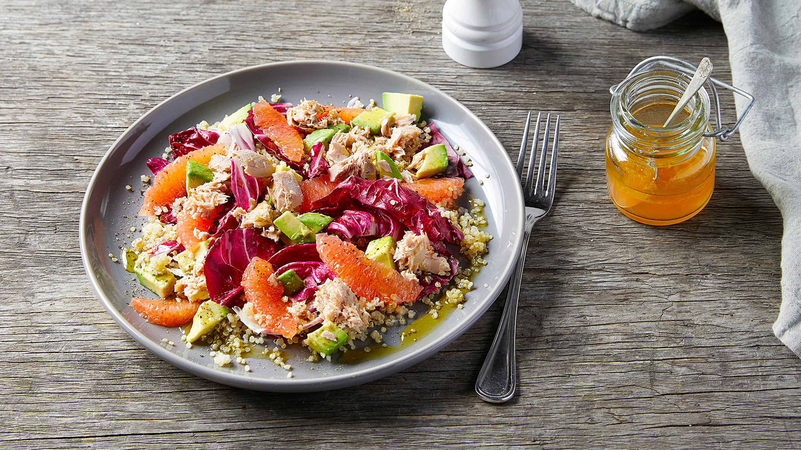 A colourful plate of radicchio, grapefruit and tuna salad sits on a grey plate on a rustic wooden table.