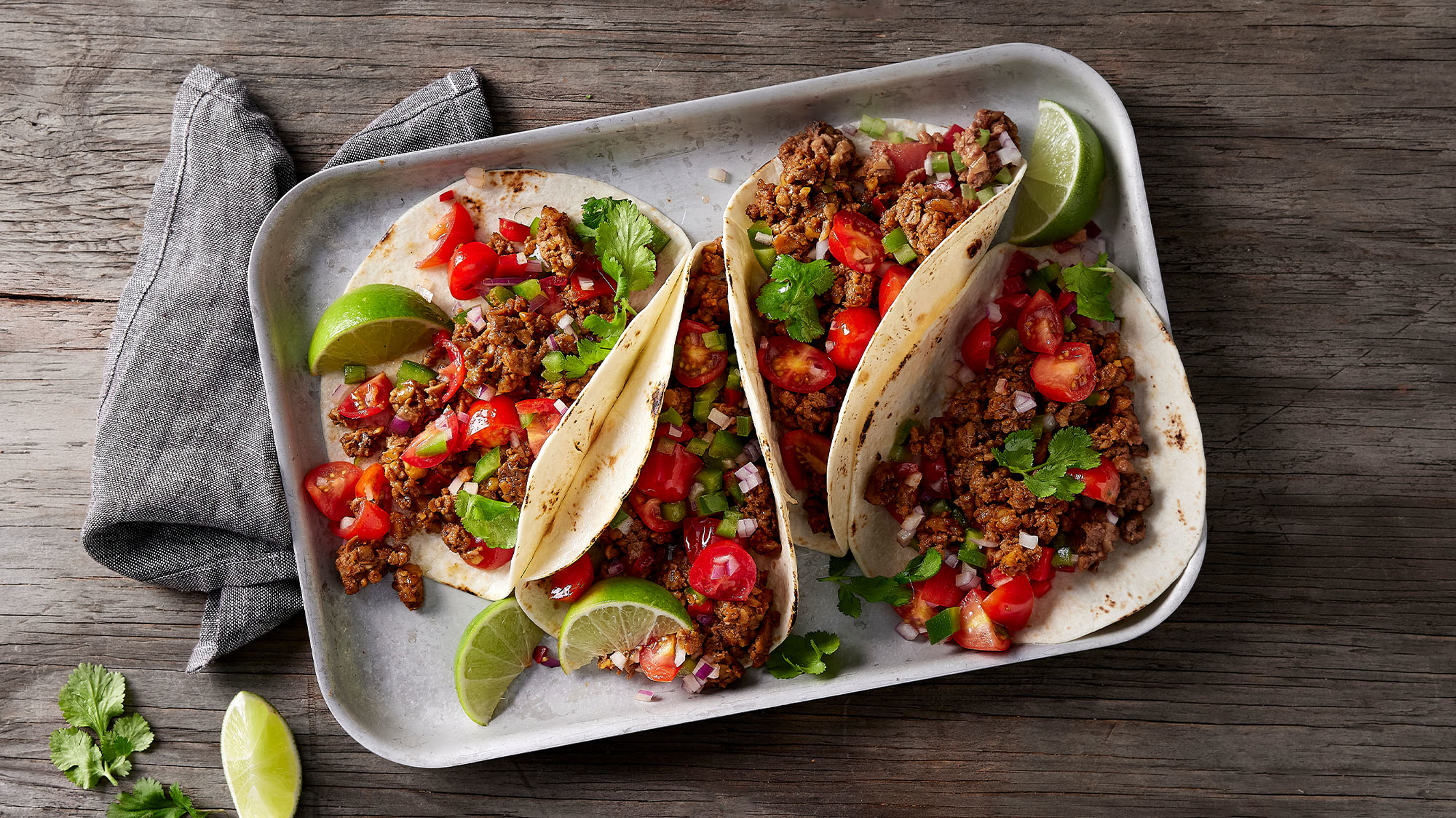 A ceramic tray of 4 of Centr's Spicy Walnut Tacos sits on a rustic wooden table.