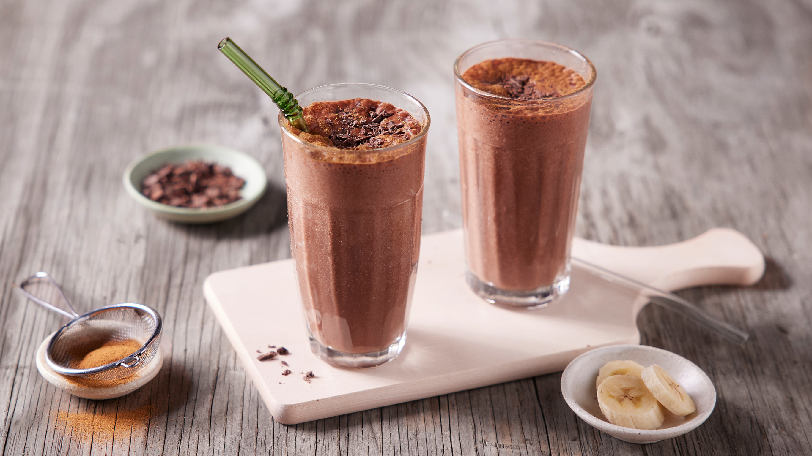 Two tall glasses of Centr's triple chocolate super smoothie sit on a white wooden cutting board.