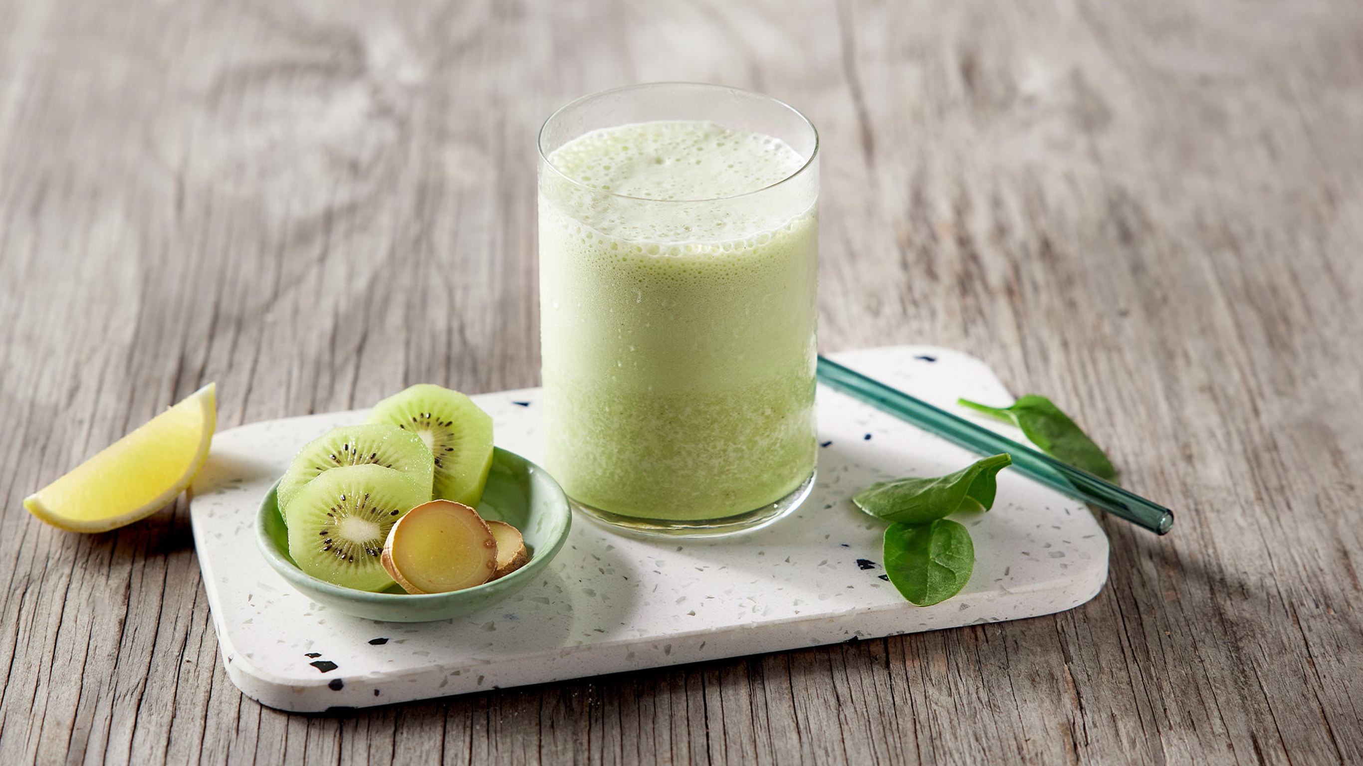 A glass of Kiwi Coconut Rejuvenating Smoothie, from the Centr meal plan, sits on a table with a small bowl of condiments.