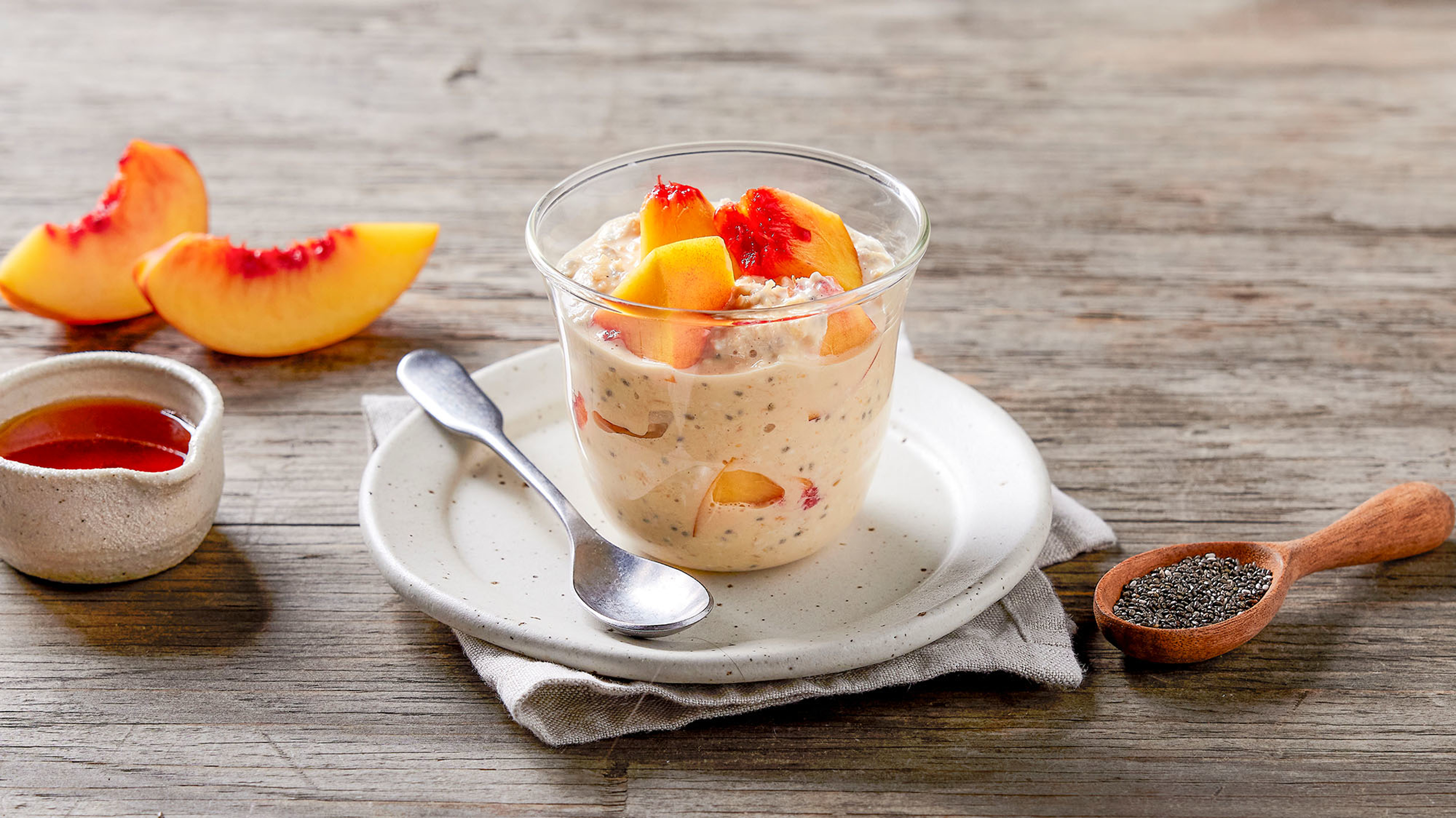 A glass tumbler of Peaches & Cream Overnight Oats sits on a small plate.