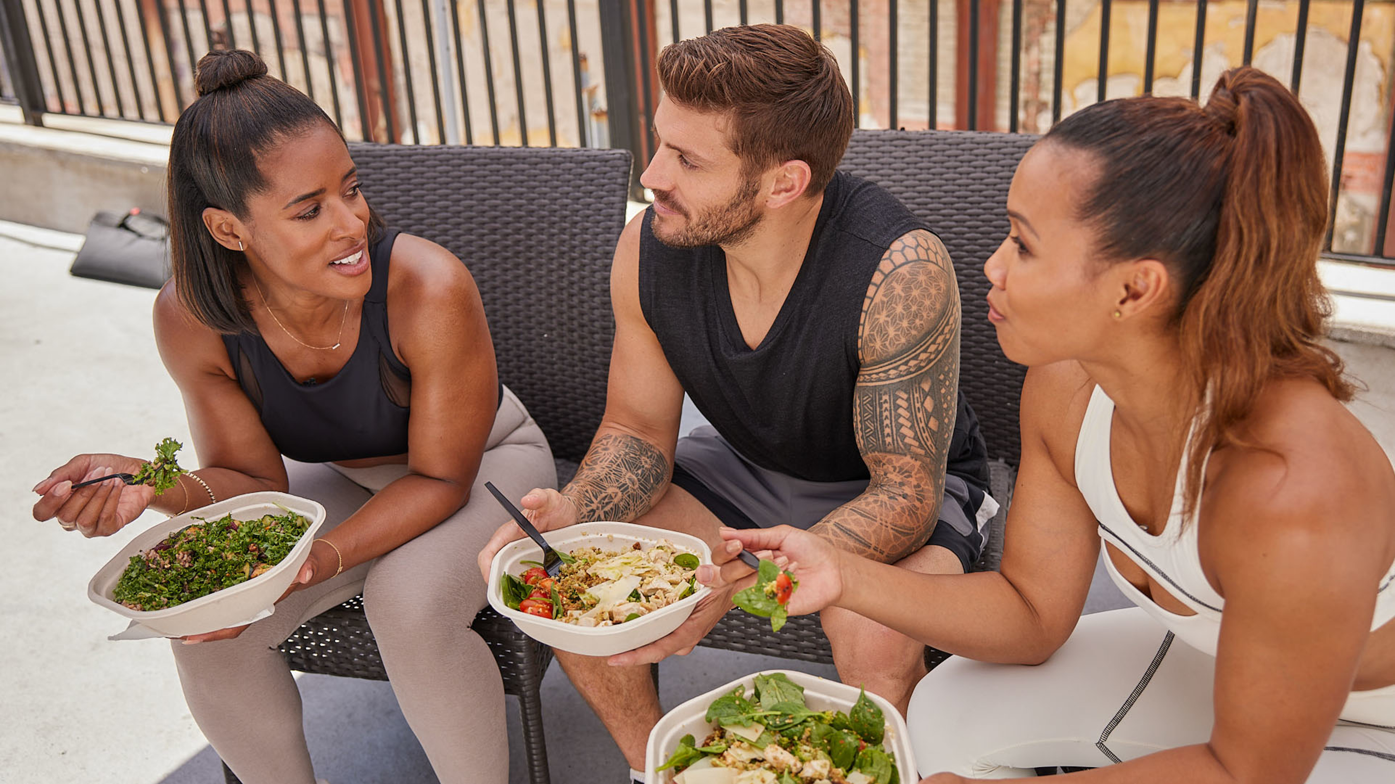 Centr trainers Ingrid Clay, Luke Zocchi and Maricris Lapaix sit together, eating green salad bowls.