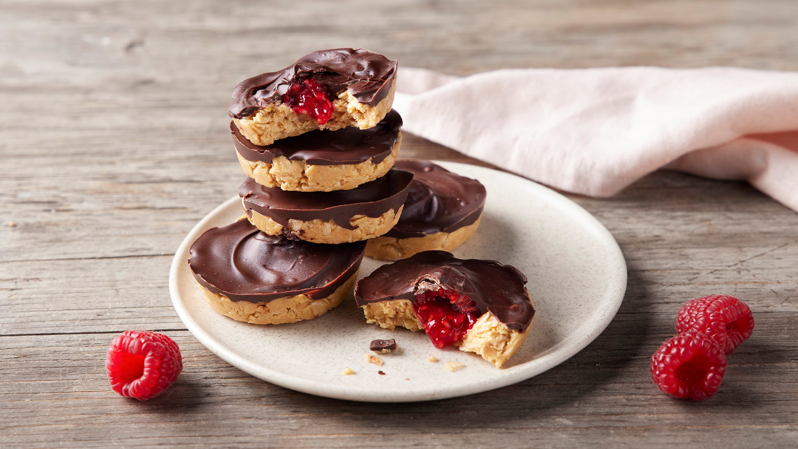 A plate of Choc PB & J Protein Cups rests on a wooden table with a linen napklin on the side.