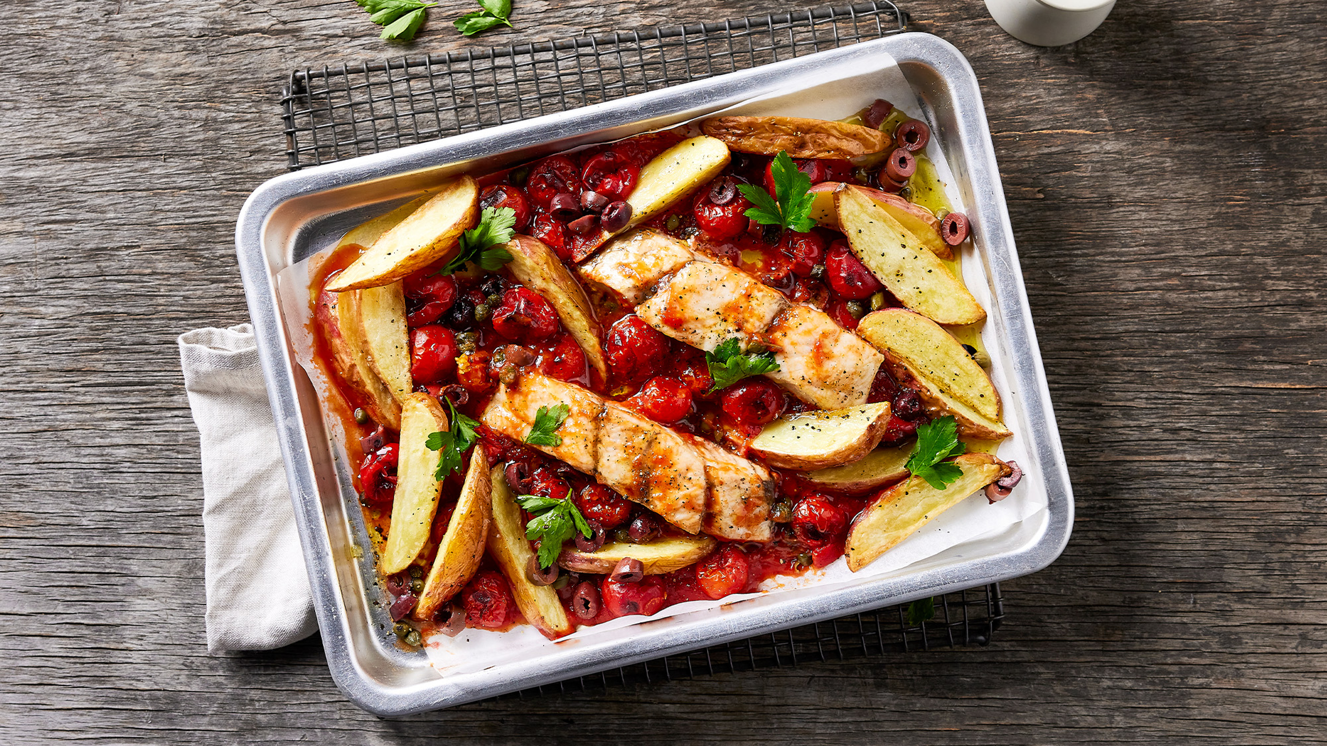 A tray of Dan’s Italian-style Fish & Potato Sheet-pan rests on a rack on a wooden table.