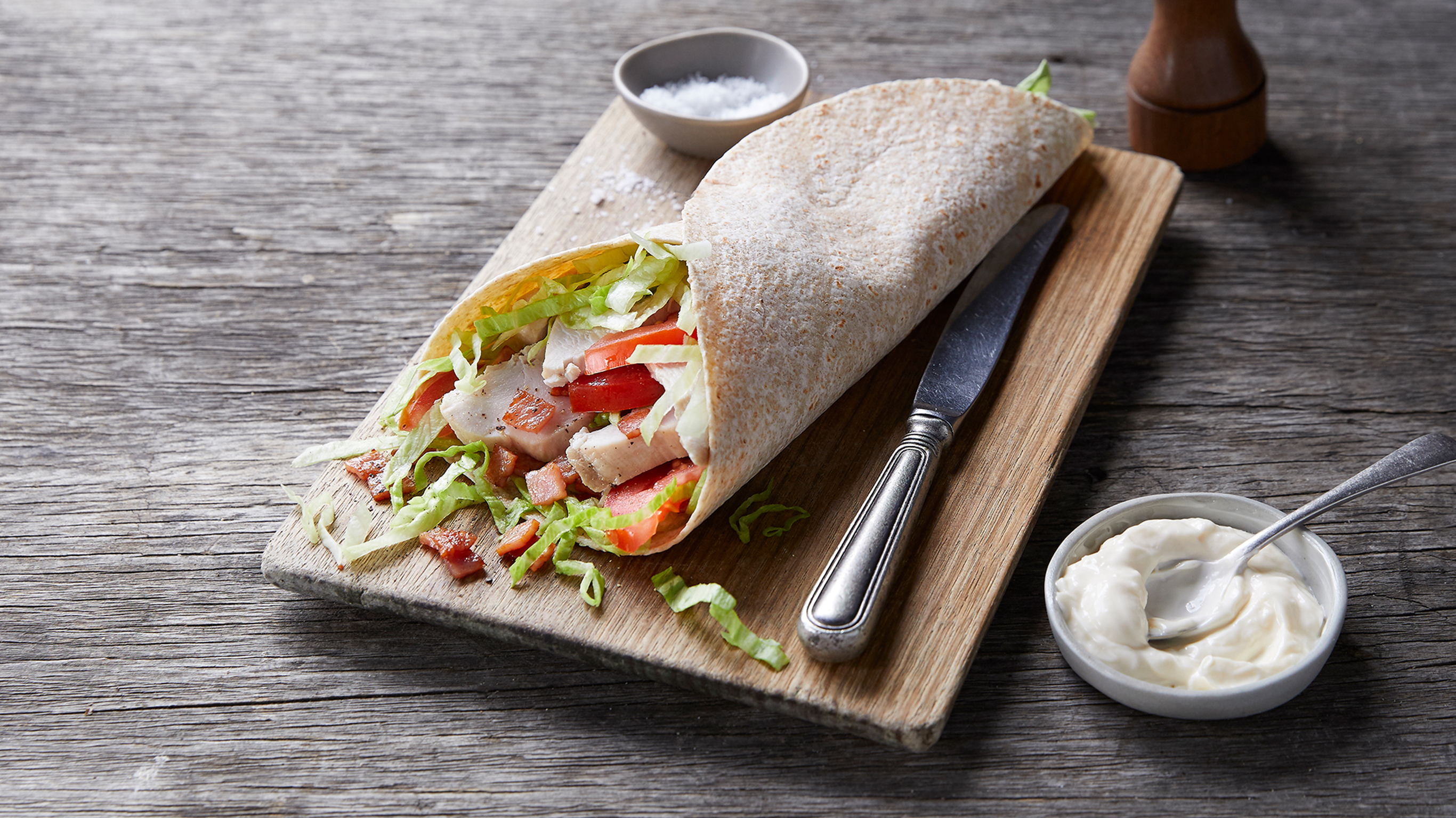 Centr's leftover turkey and crispy bacon wraps sits on a wooden board, with a small dish of mayonnaise on the side.